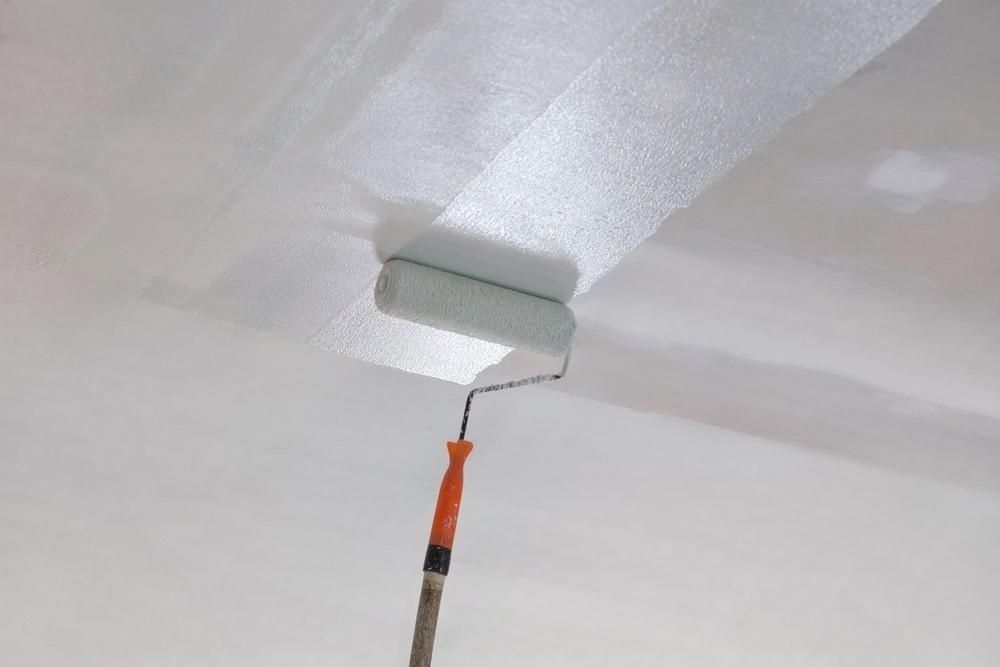 A paint roller is being used to paint a white ceiling.