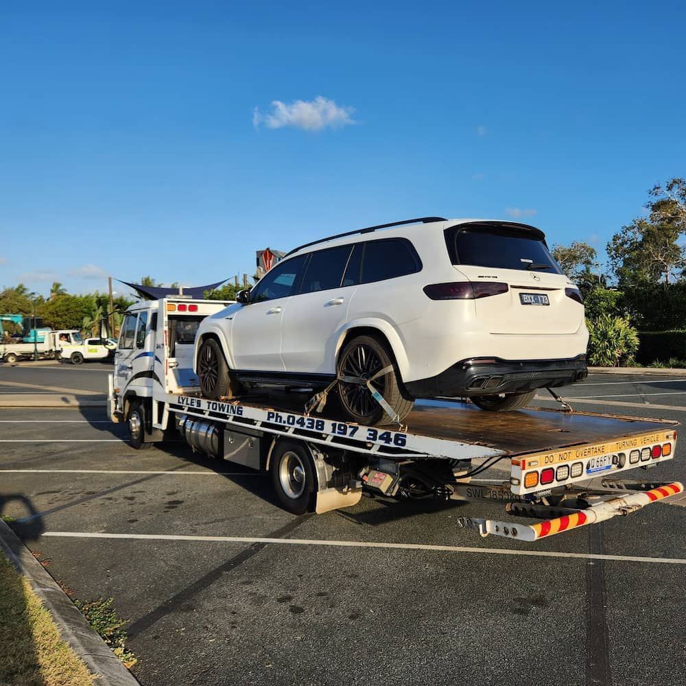 A White SUV is Being Towed by a Tow Truck in a Parking Lot — Lyle's Towing In Little Mountain, QLD