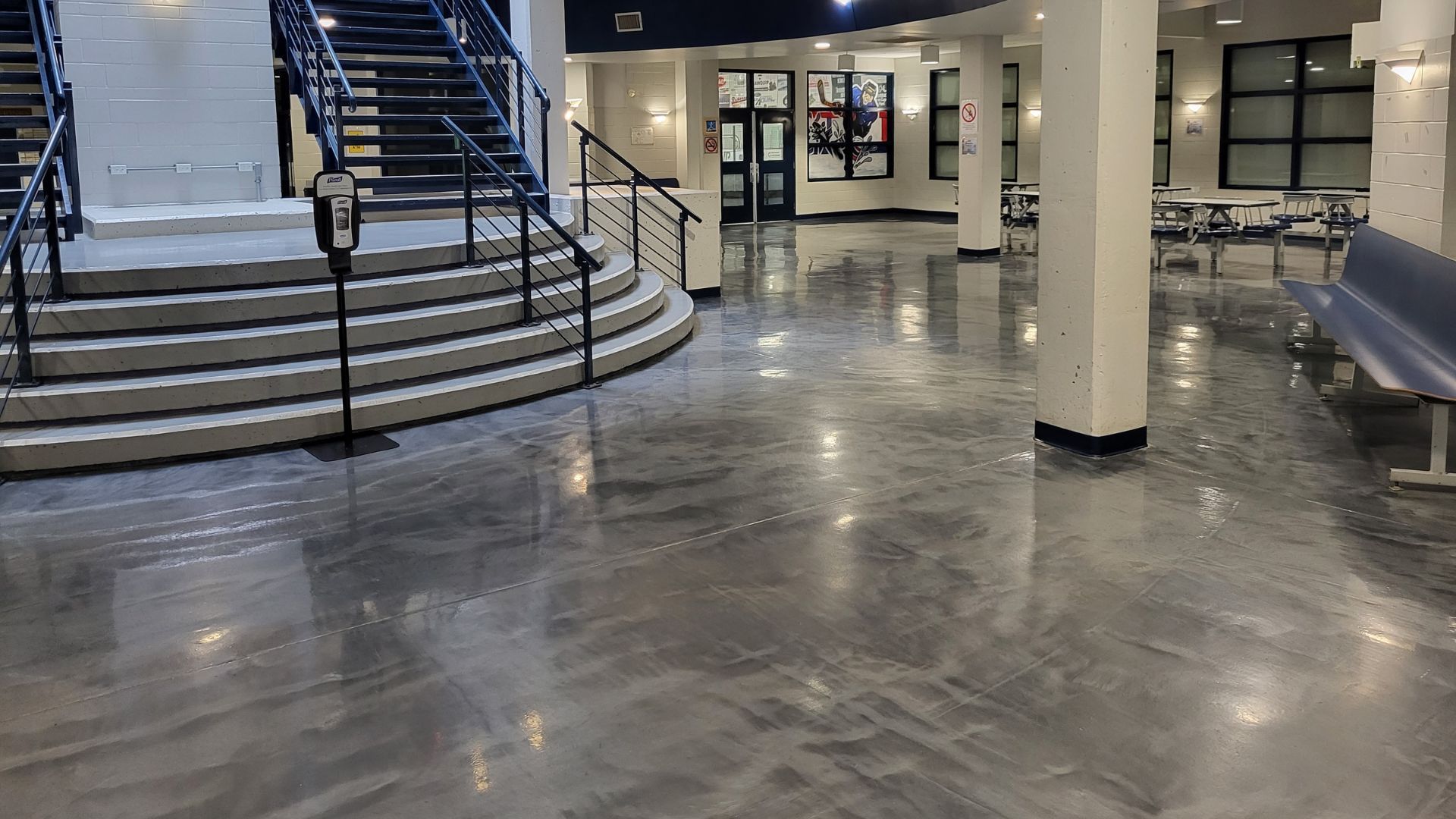 Polished gray floor in a building lobby with stairs, columns, and benches.