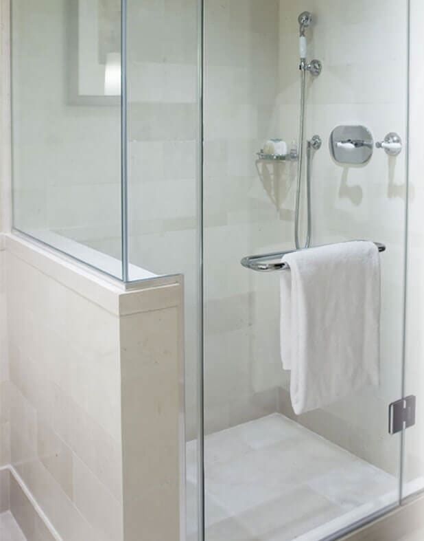 Mampara de ducha de cristal con toallero blanco colgado en el tirador.