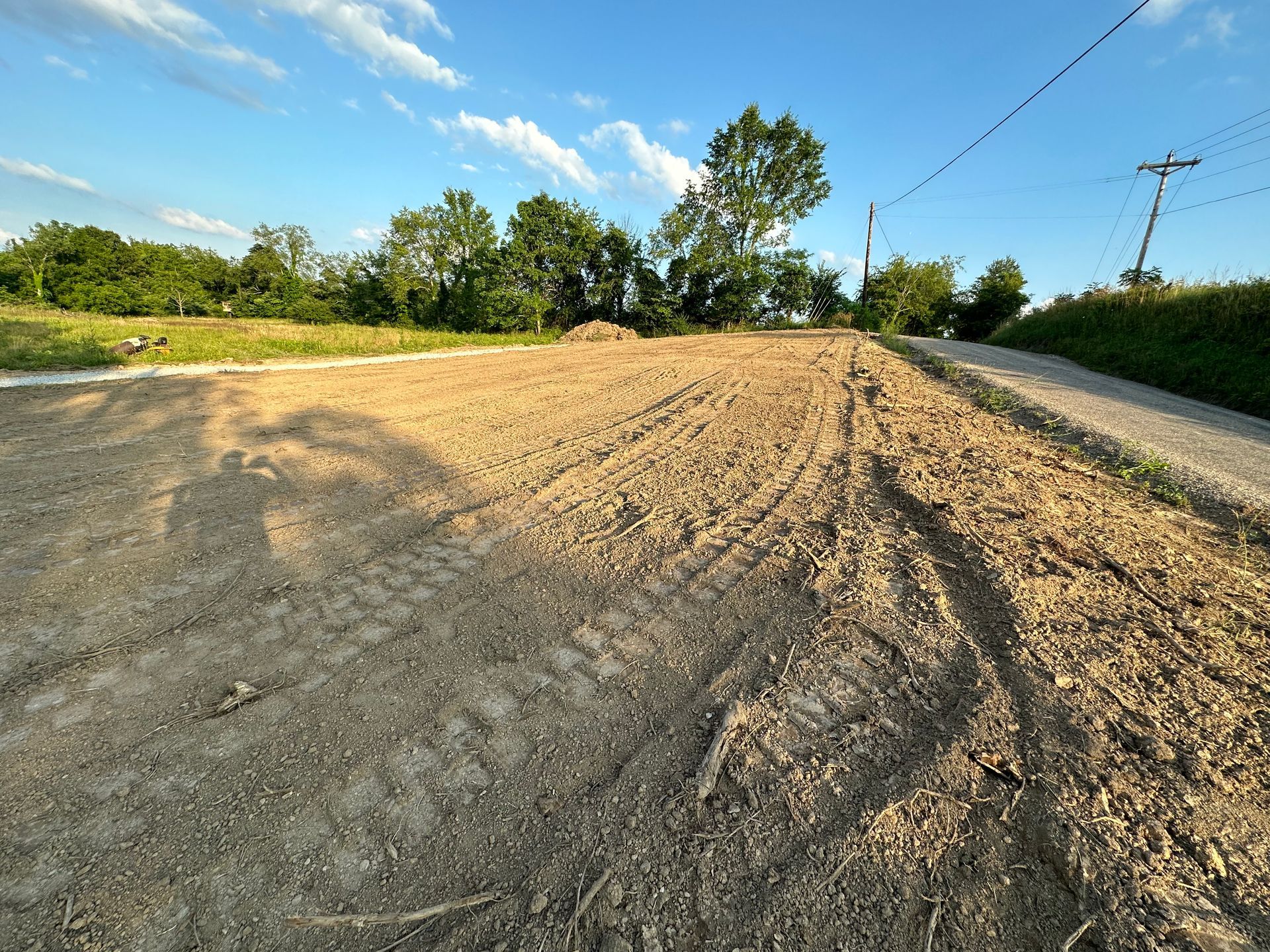 A dirt road going through a field with trees in the background.