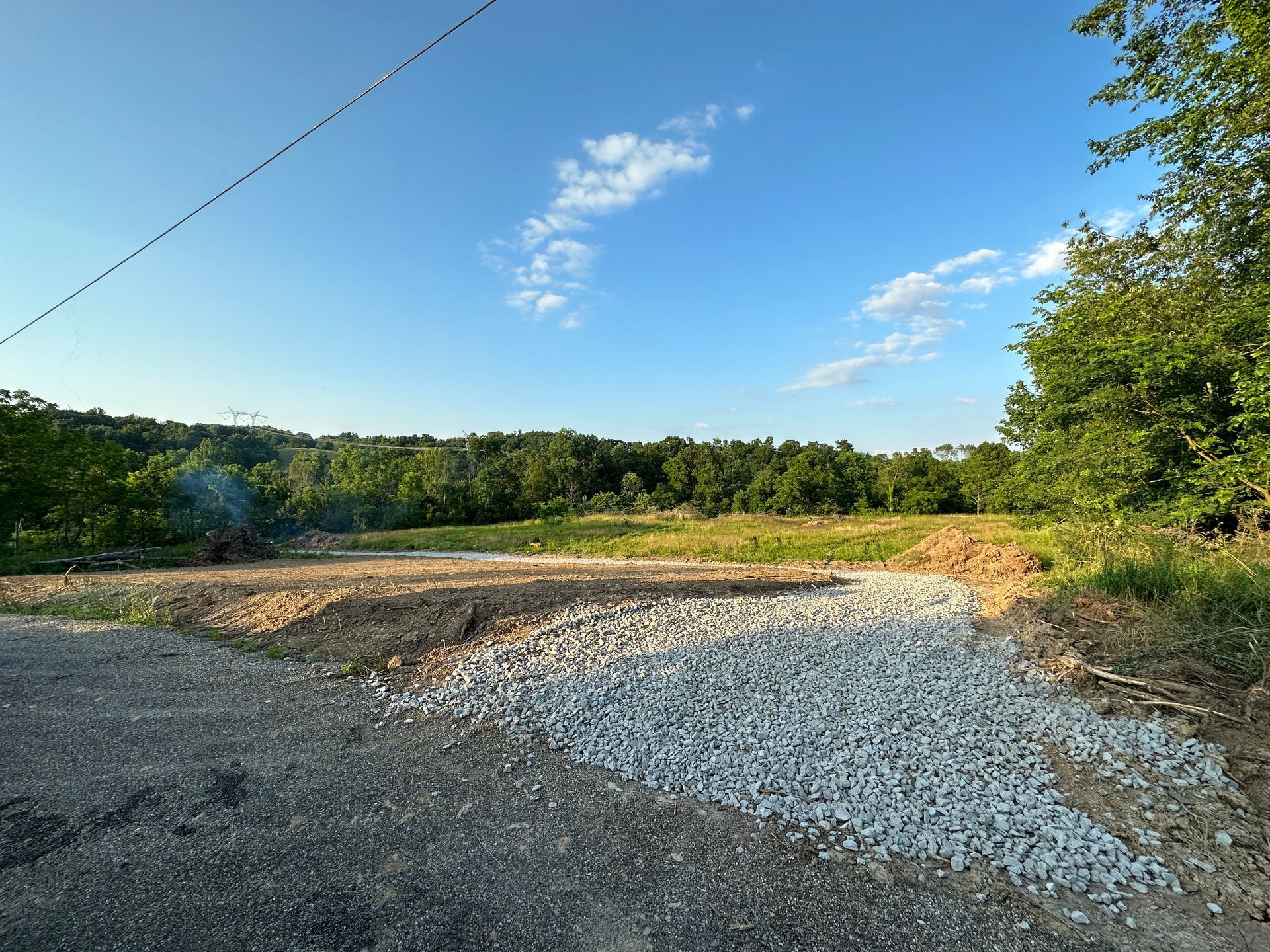 A gravel road leading to a field with trees in the background.