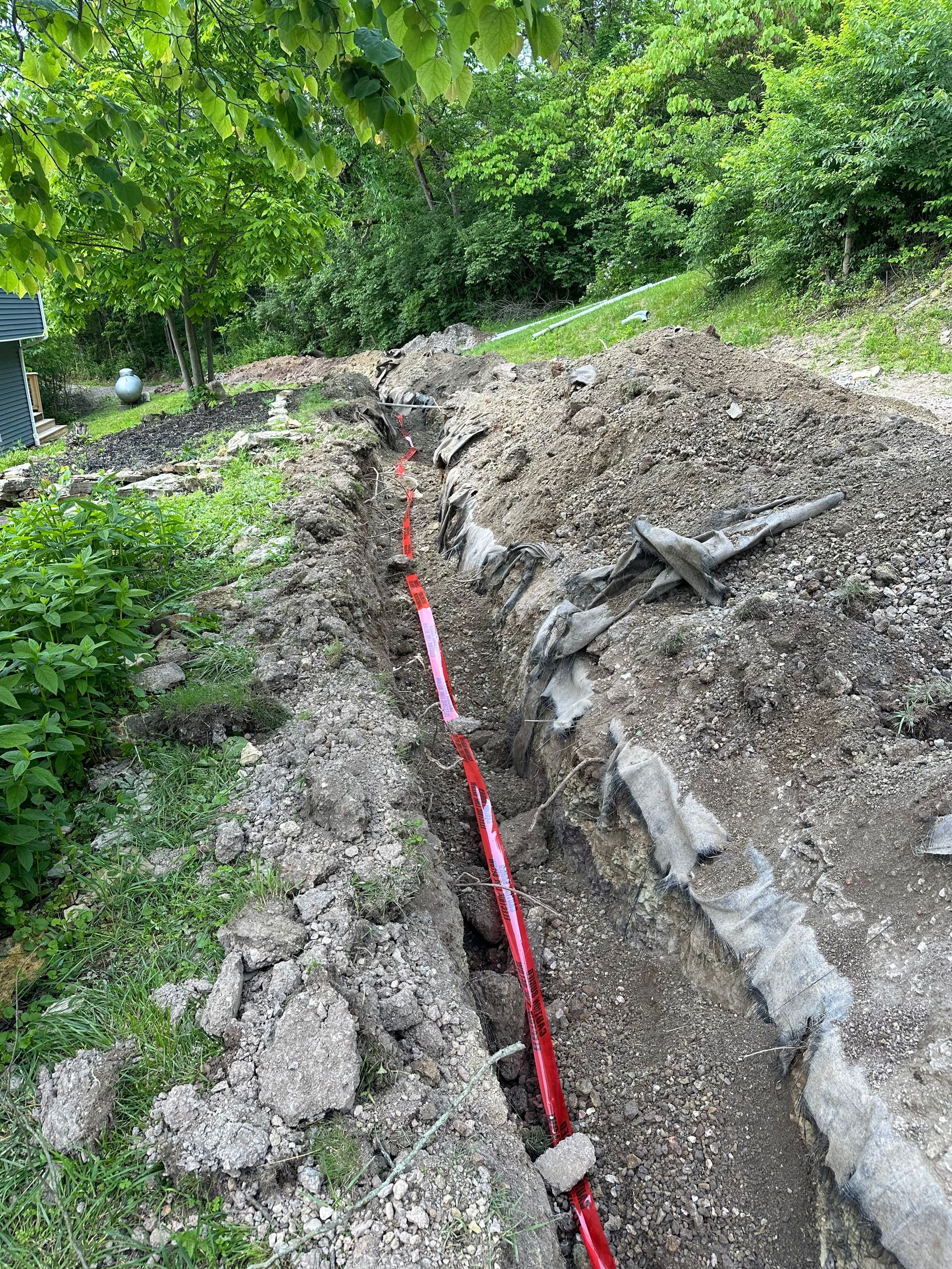 A red pipe is laying in the dirt in a trench.