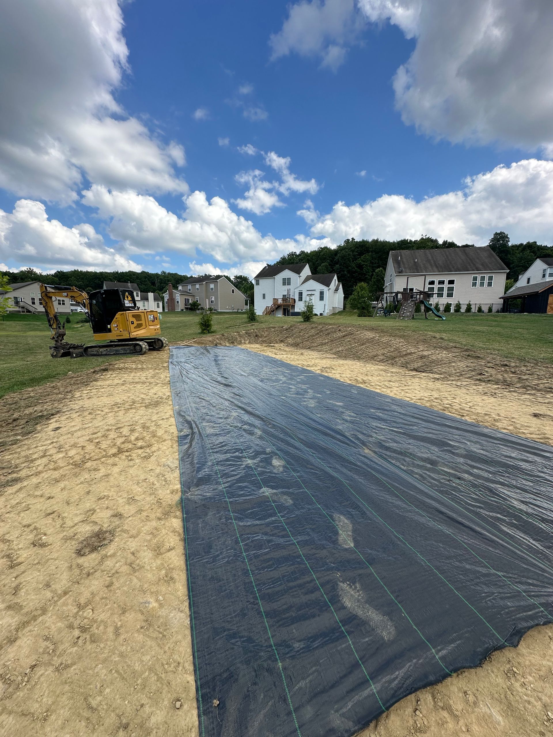 A black tarp is covering a dirt road in a residential area.