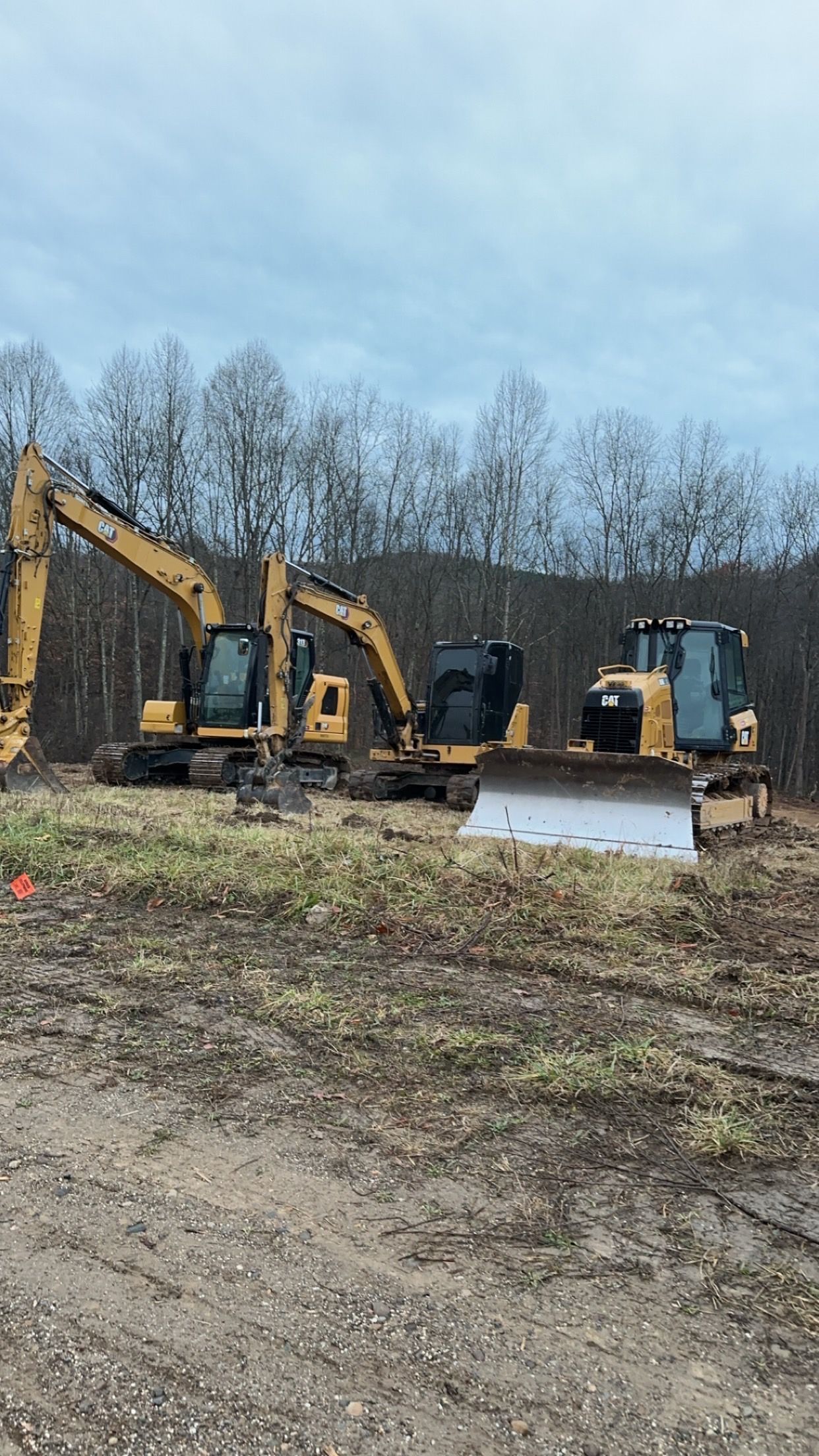 Three construction vehicles are parked in a dirt field.