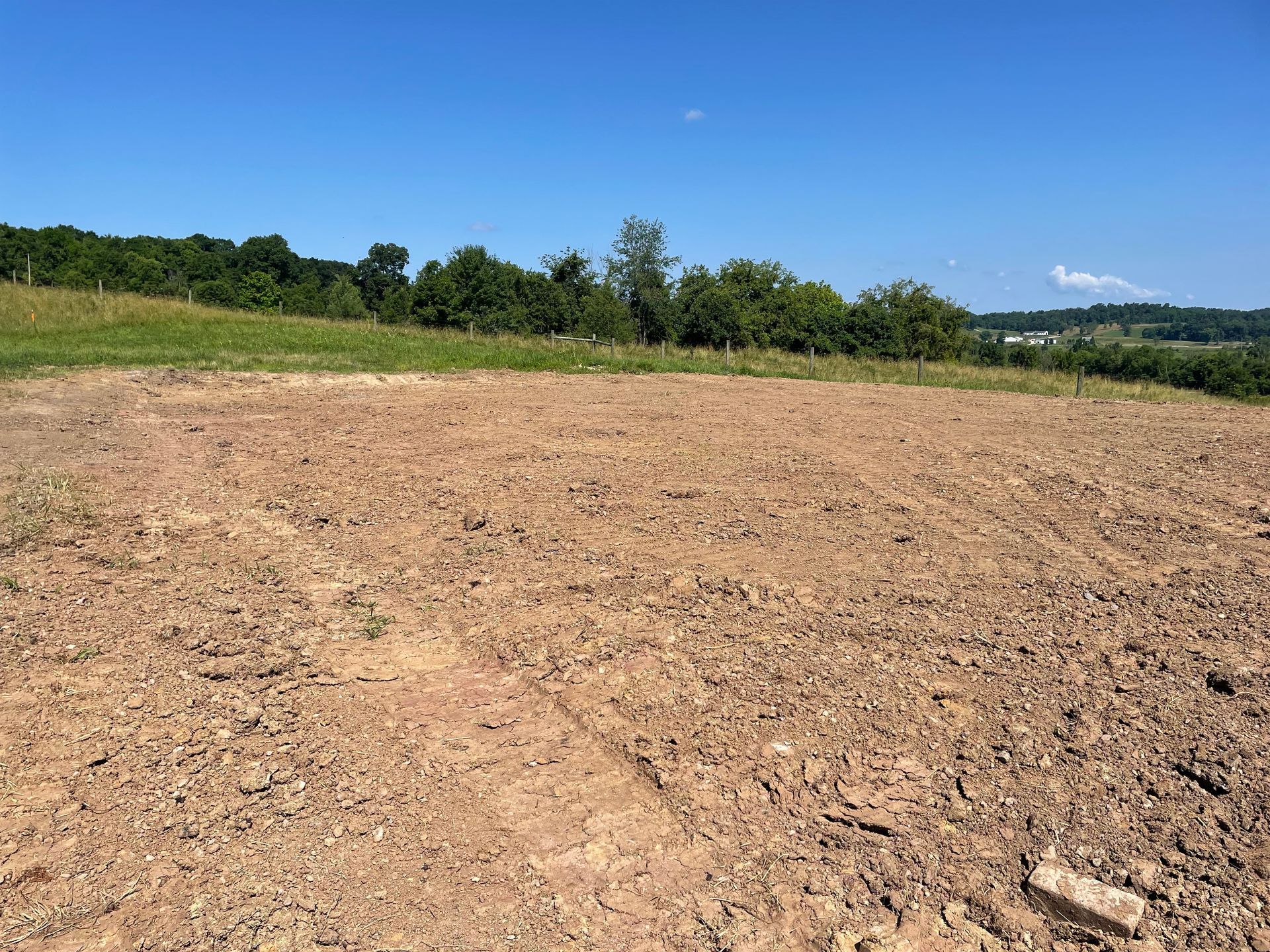 A dirt field with trees in the background and a blue sky