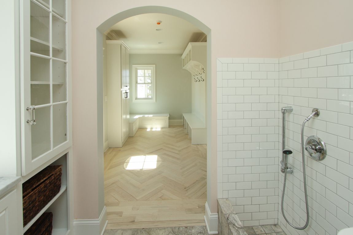 Bathroom interior with arched doorway, white cabinetry, herringbone floor, and tiled shower.