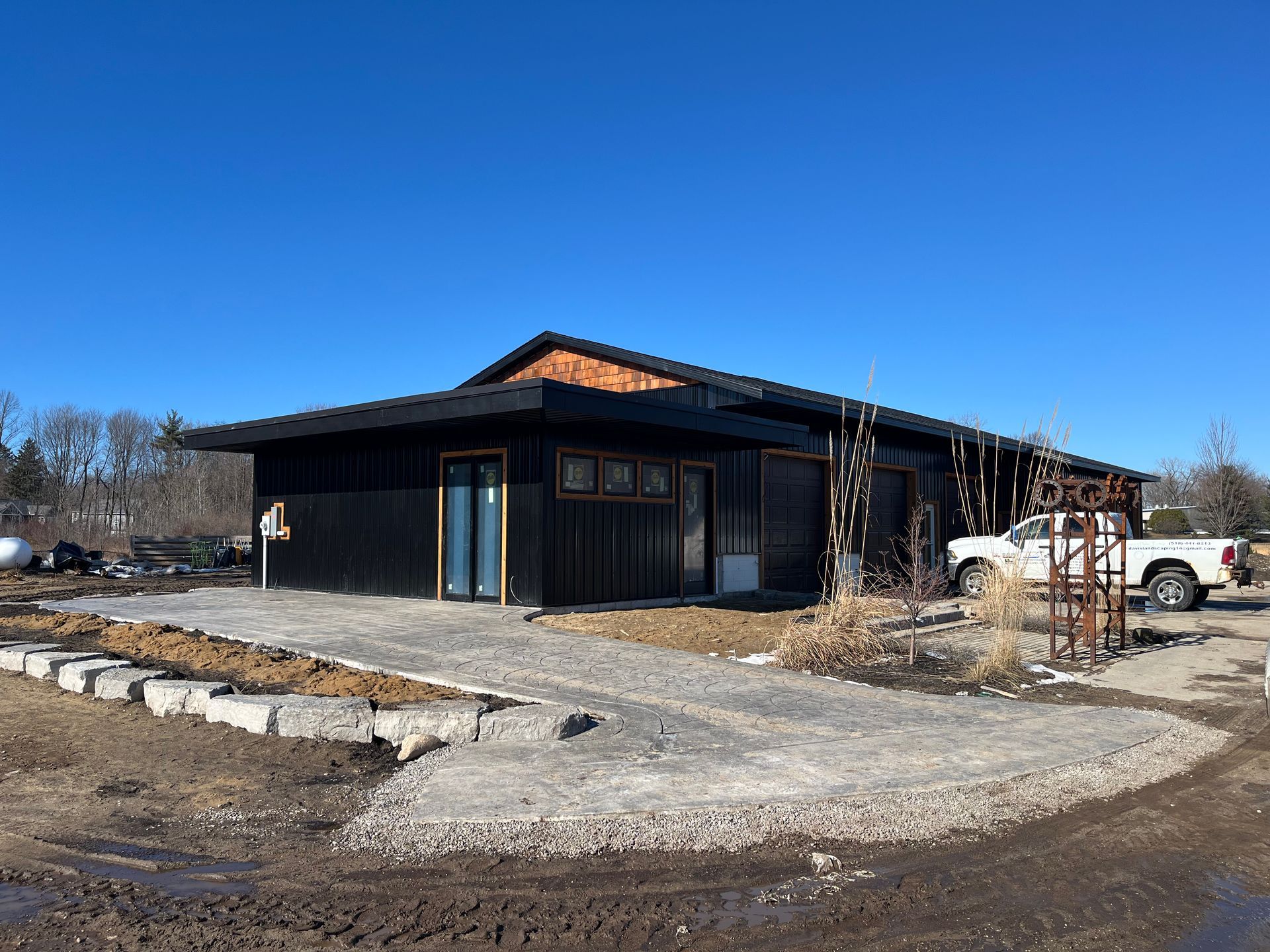 Black building with a ramp, gravel path, and a white truck parked nearby, against a clear blue sky.