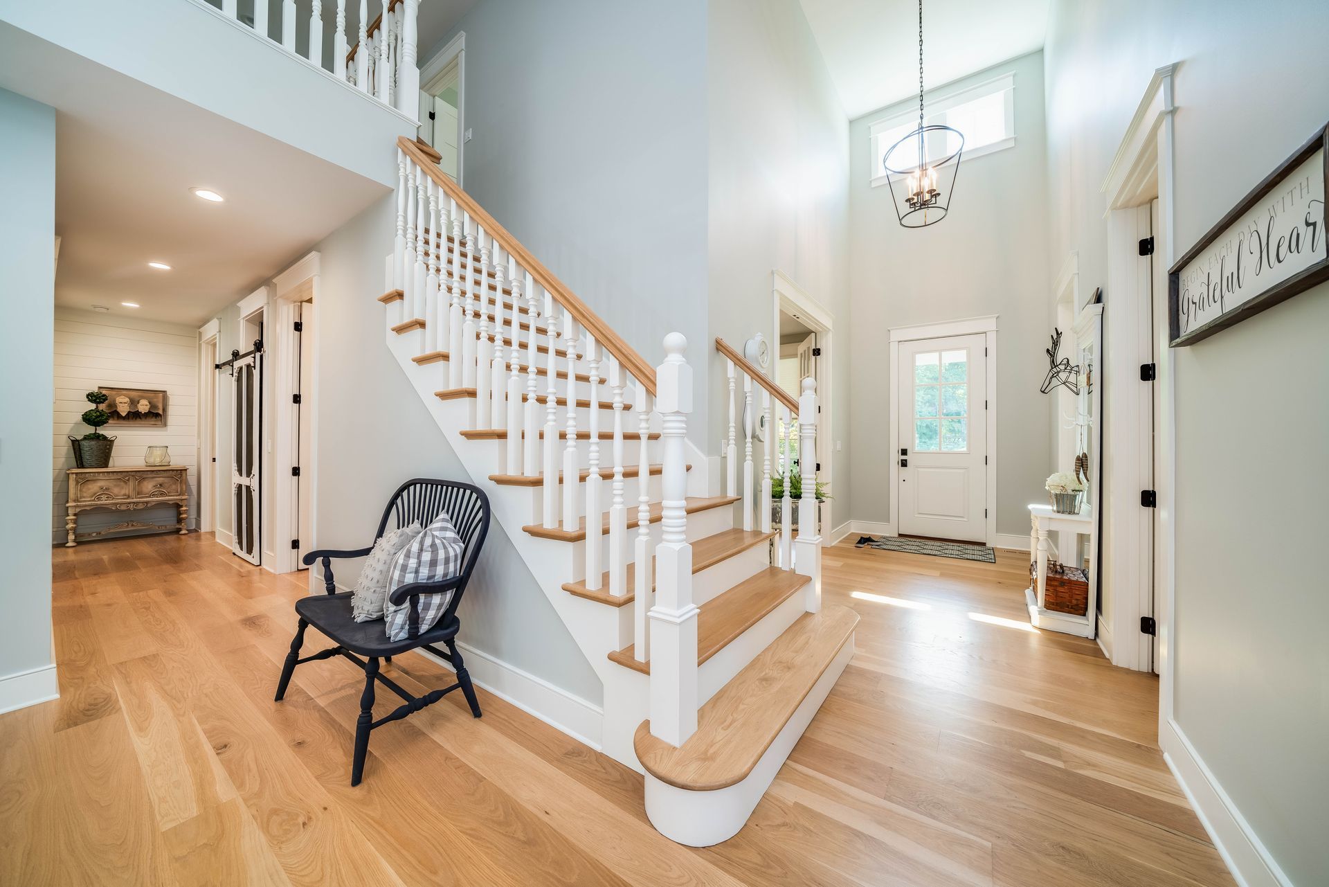 Light-filled entryway with wood floors, white staircase, and black chair. Interior of a home with light blue walls.