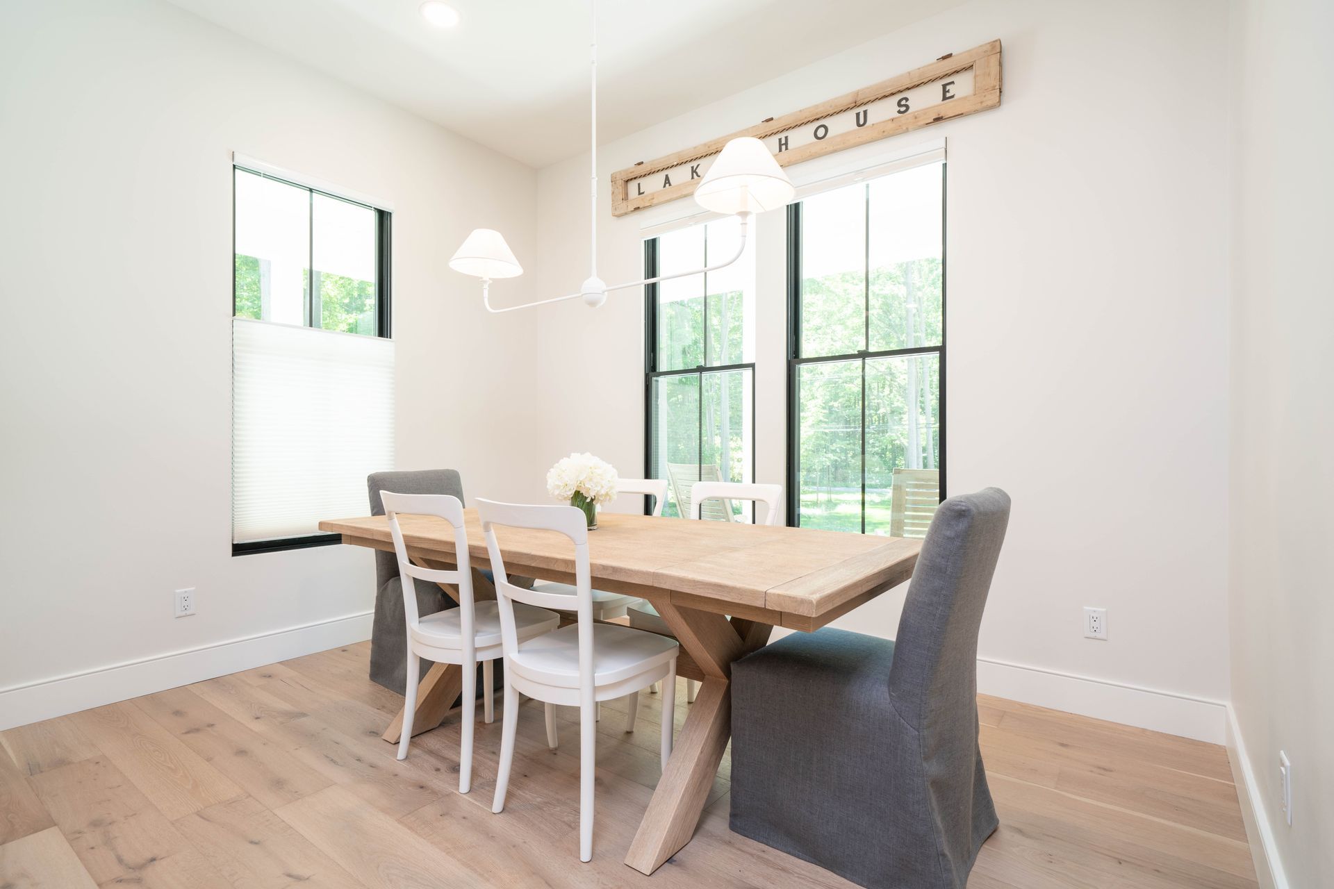A dining room with a wooden table and chairs and two windows.