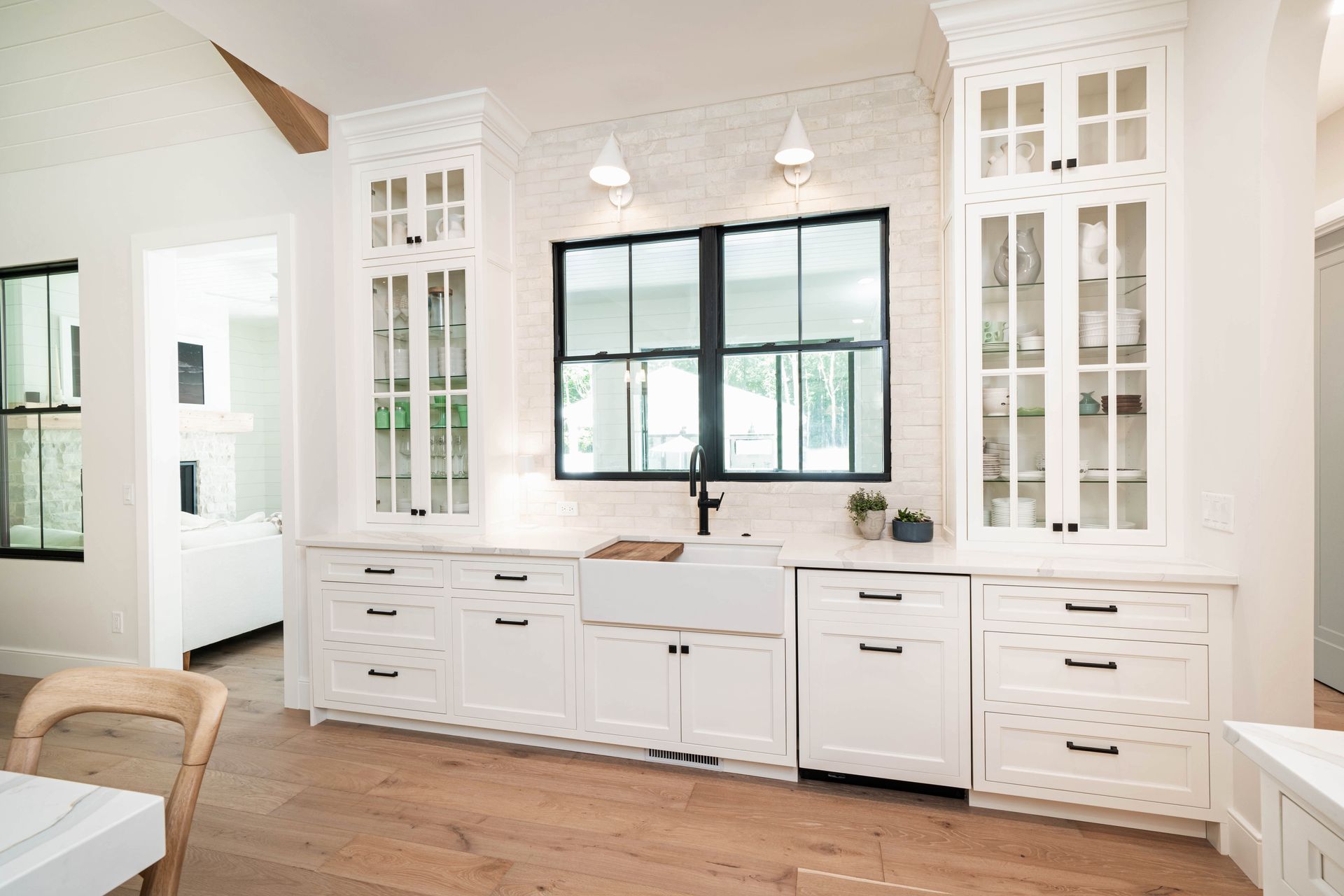A kitchen with white cabinets , a sink , and a large window.