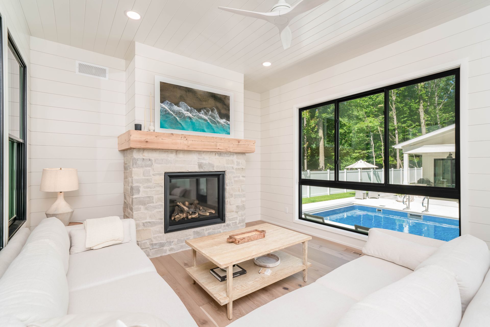 A living room with a fireplace and a swimming pool in the background.