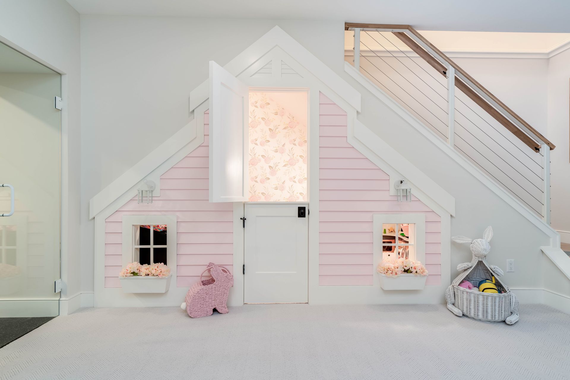 A pink and white playhouse is under the stairs
