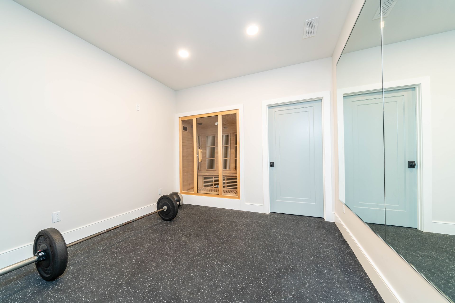 A gym with a barbell on the floor and a large mirror.