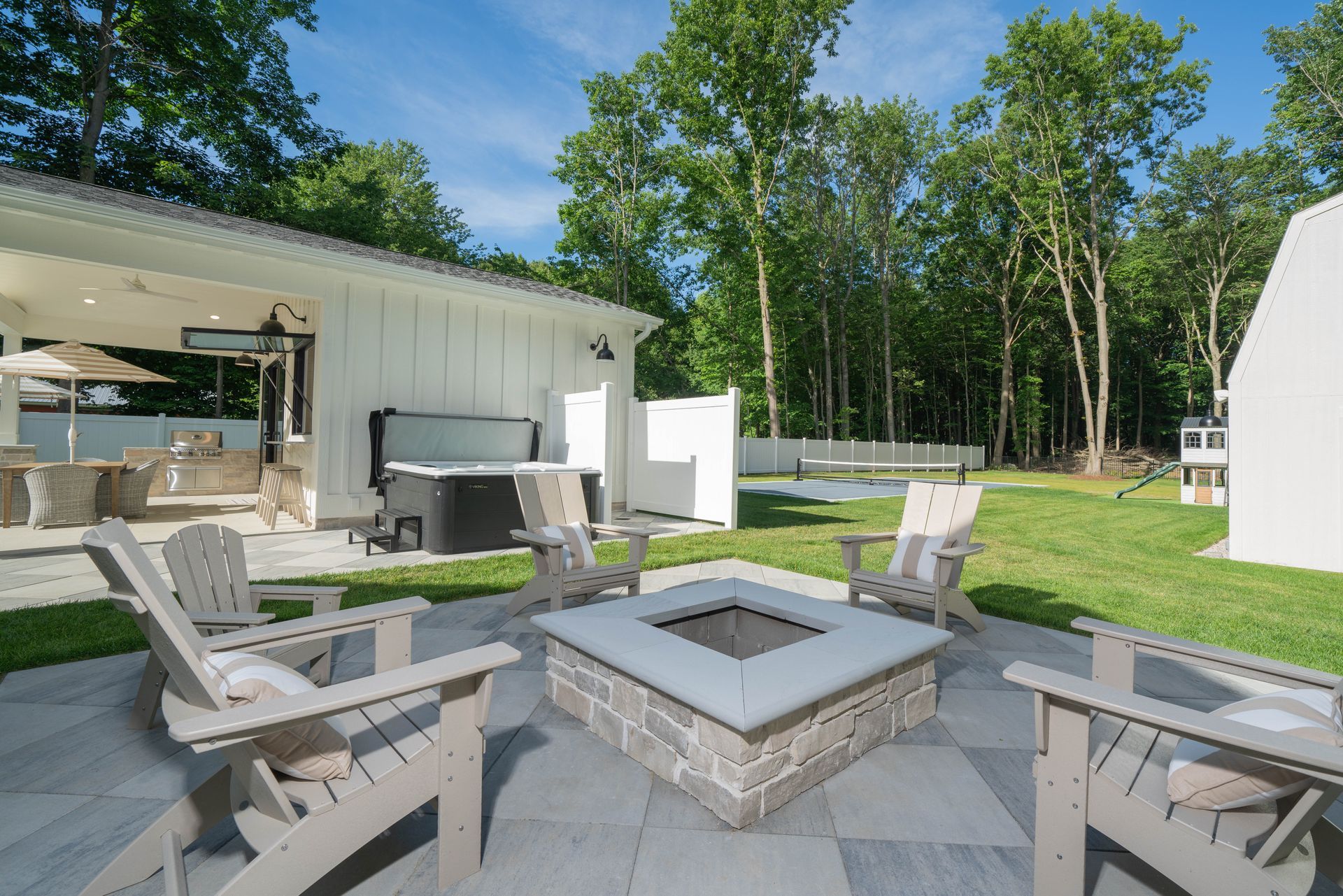 A patio with a fire pit and chairs in front of a house.