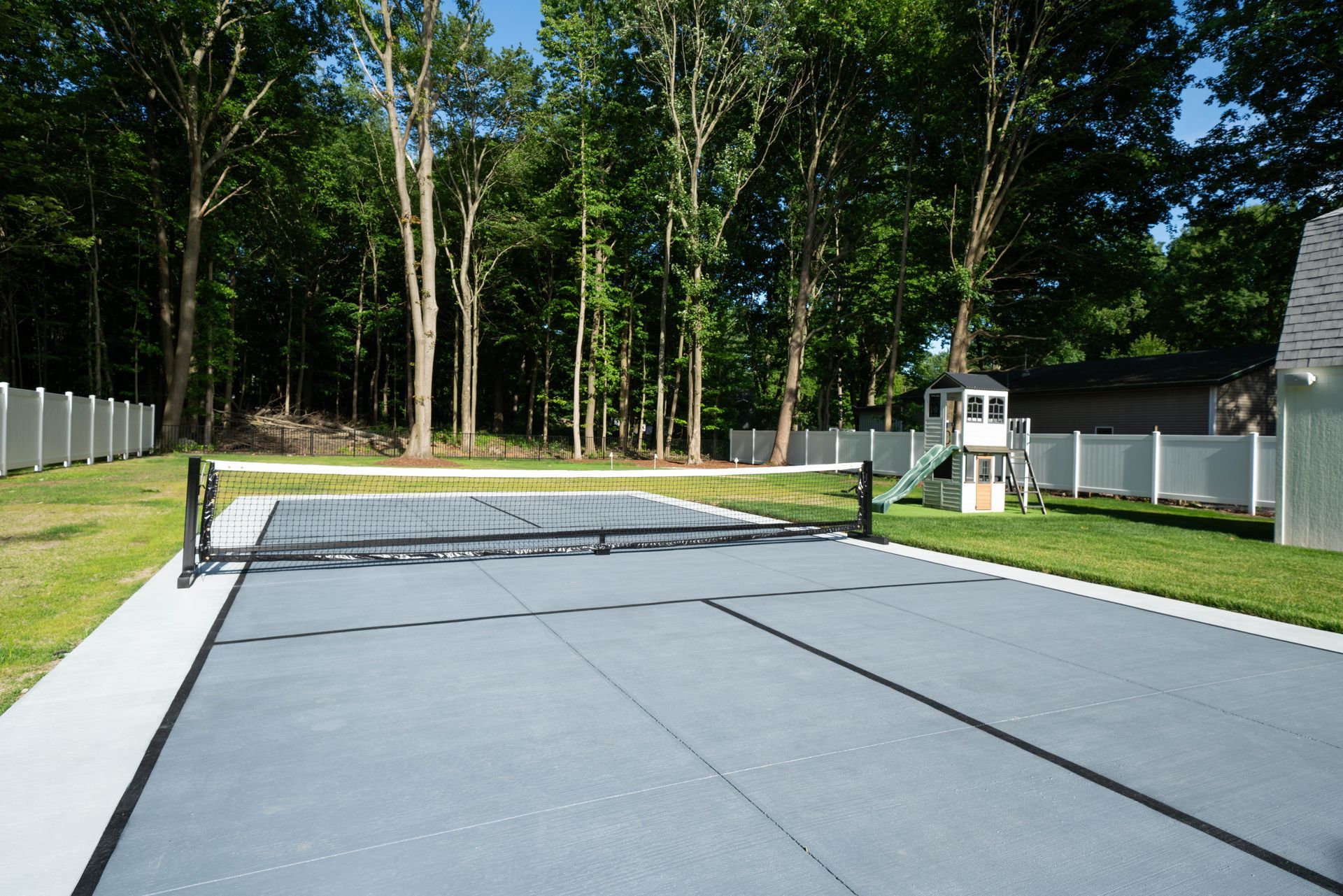 A tennis court in a backyard with trees in the background