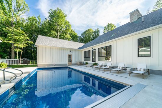 There is a large swimming pool in front of a white house.