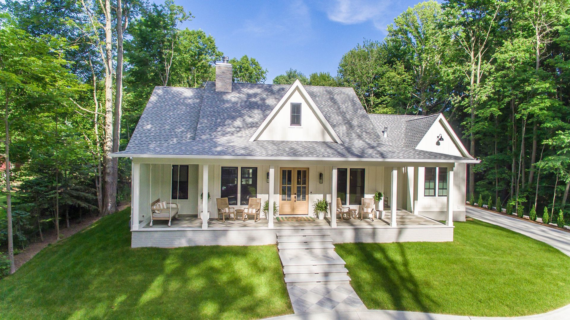 A white house with a large porch is surrounded by trees.