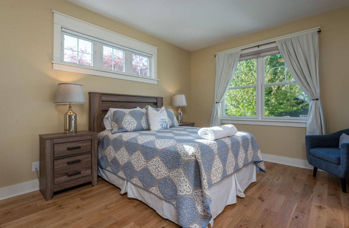 A bedroom with a king size bed, nightstand, chair and window.