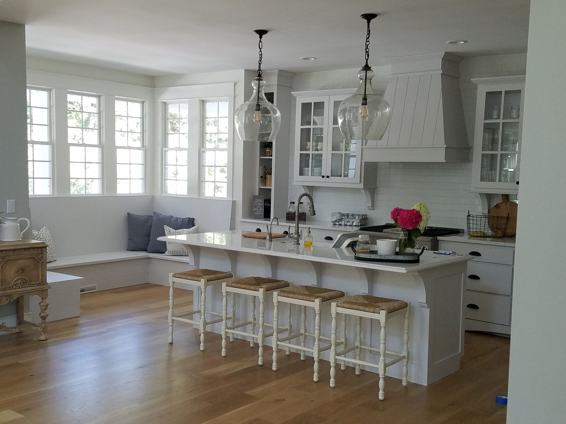 A kitchen with white cabinets , stools , and a large island.