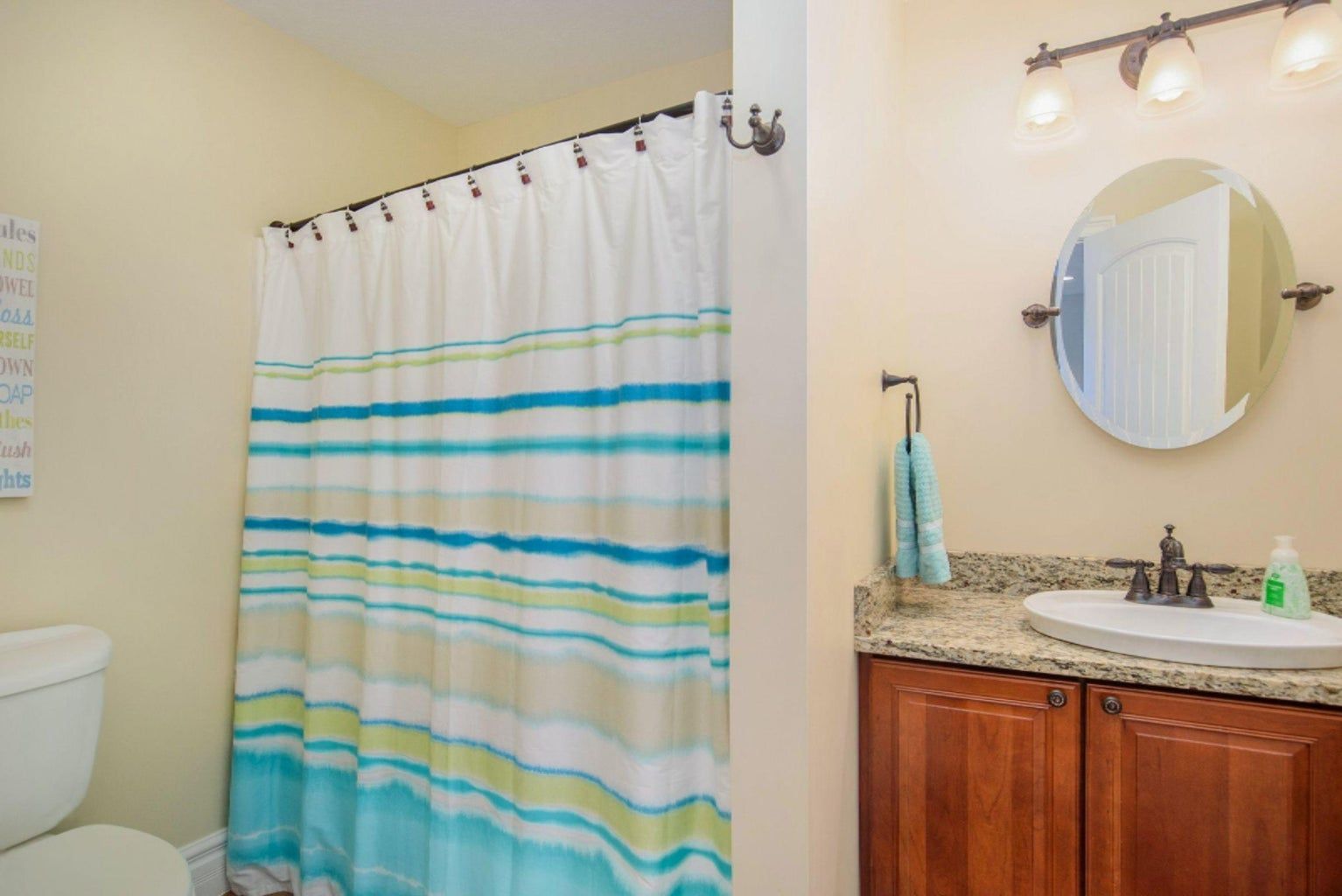 A bathroom with a shower curtain , toilet , sink and mirror.