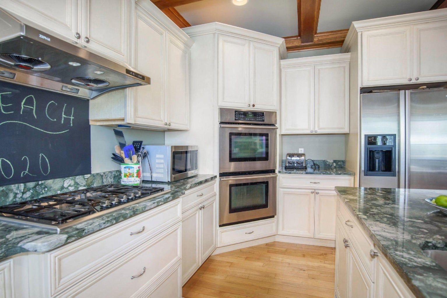 A kitchen with white cabinets and stainless steel appliances and a chalkboard that says each 020