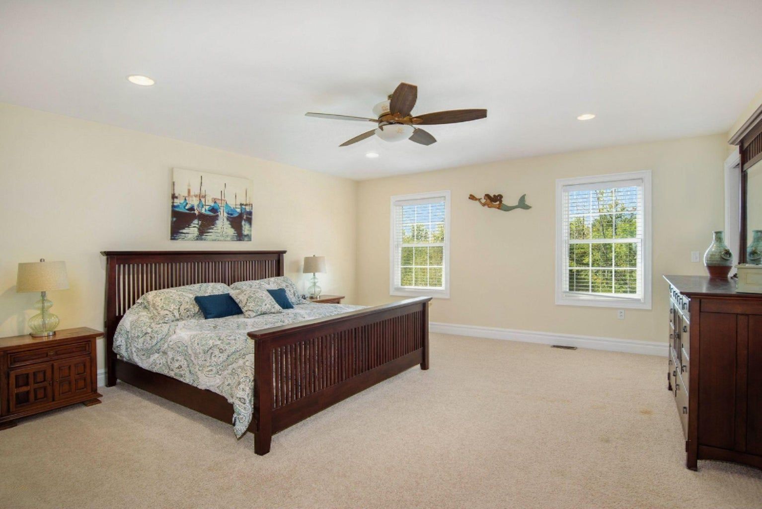 A bedroom with a bed , dresser , mirror and ceiling fan.