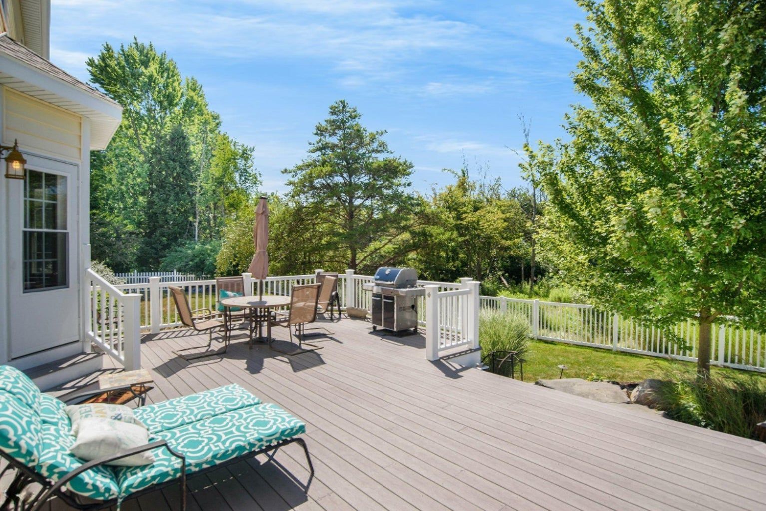 A large deck with a table and chairs and a grill.