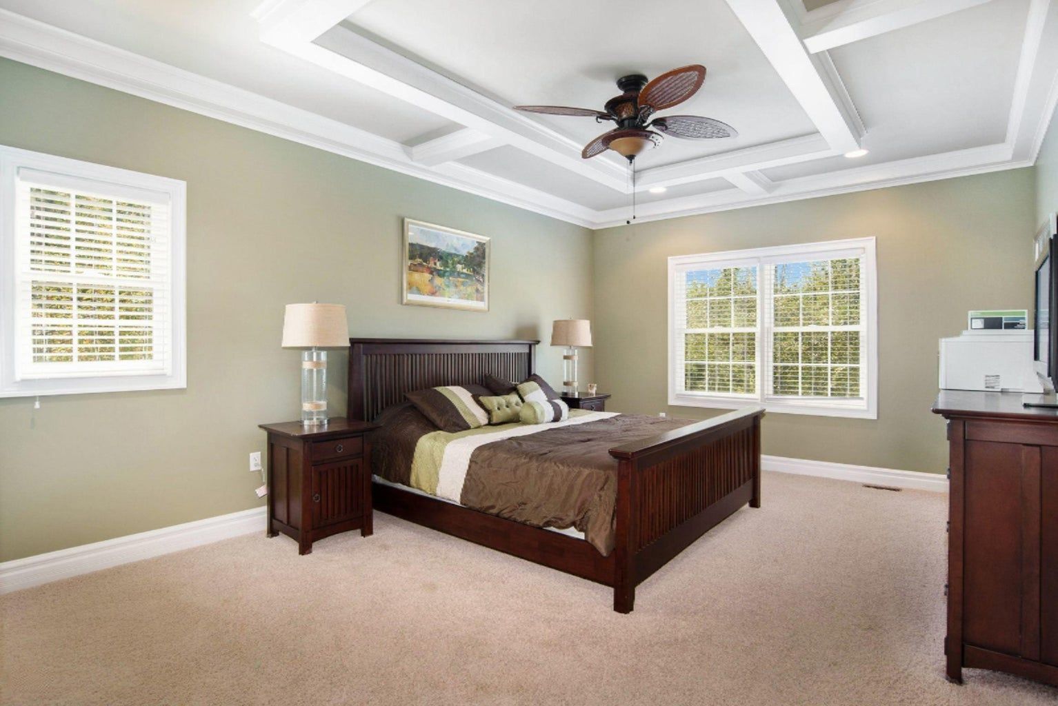 A bedroom with a king size bed , dresser , nightstand , and ceiling fan.