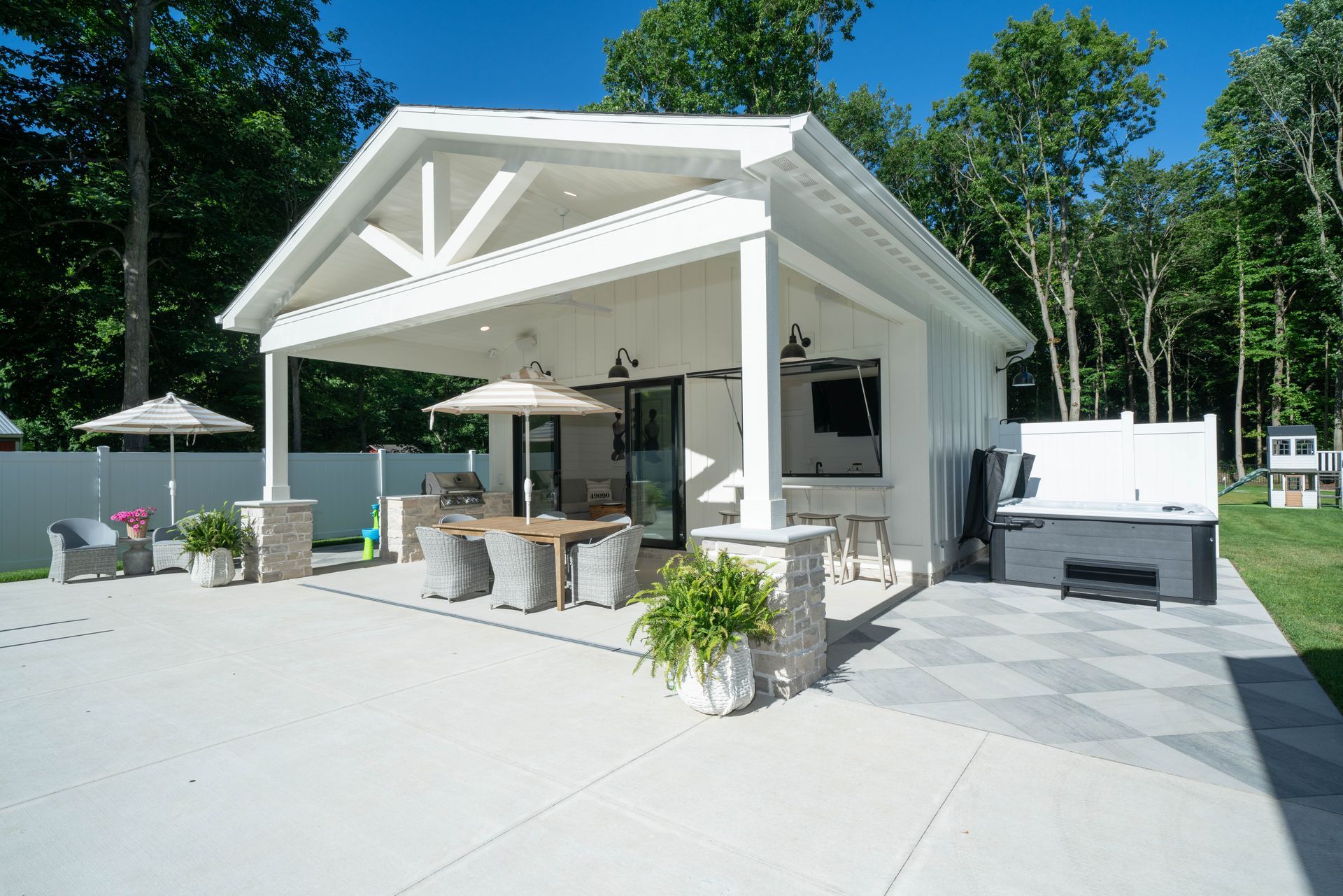 White outdoor structure with patio, dining table, bar, and hot tub.