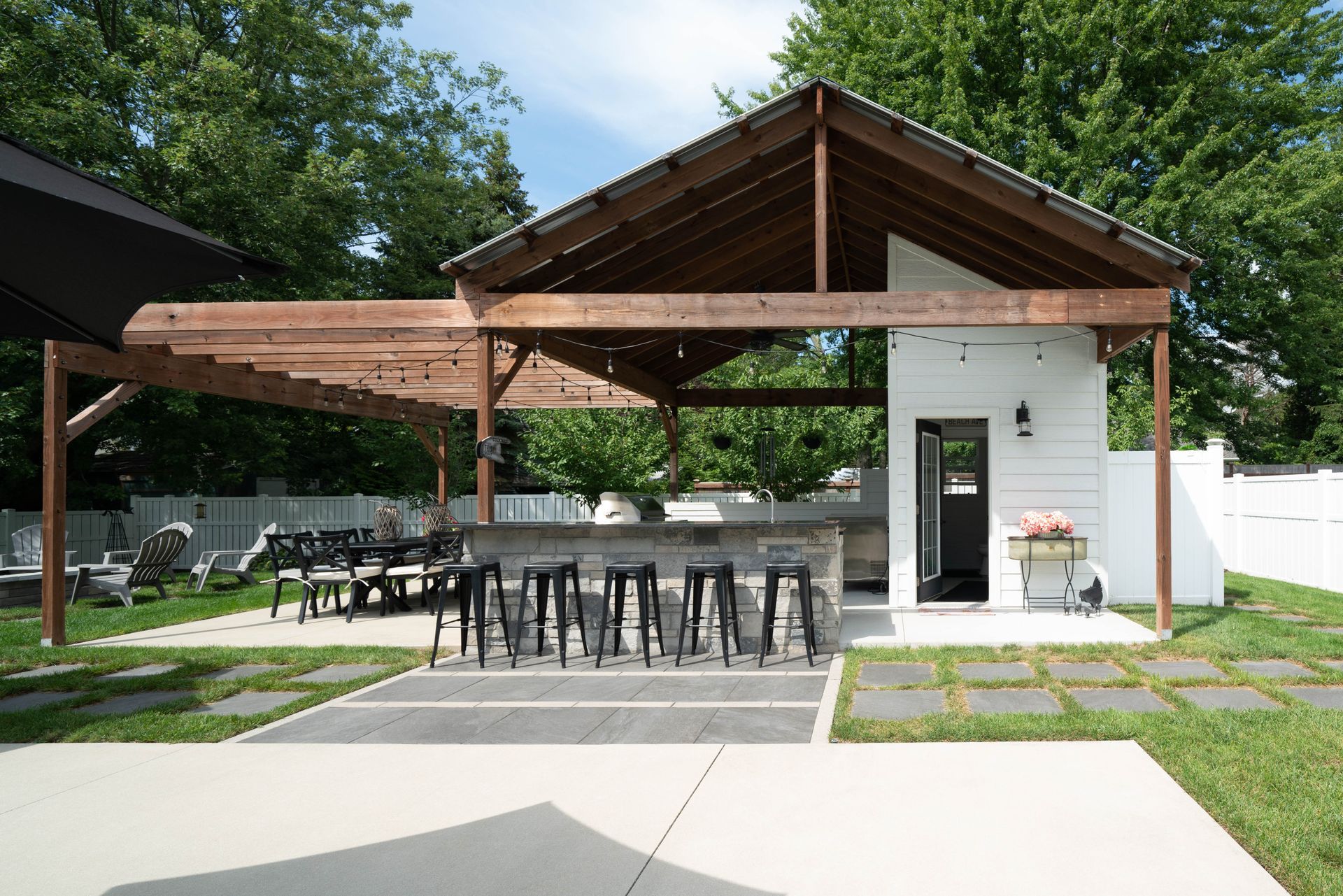 Outdoor kitchen with bar seating, wooden pergola, and white exterior.