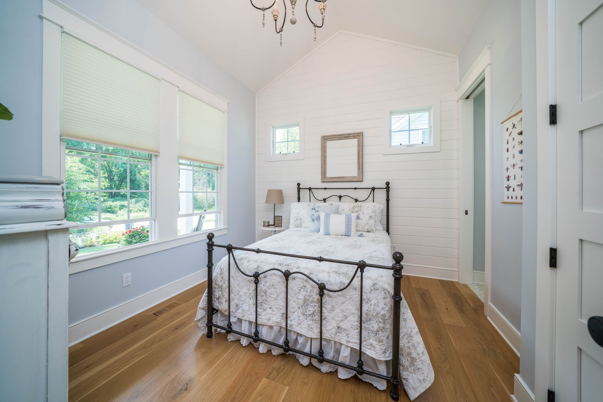 A bedroom with a bed , two windows and a chandelier.