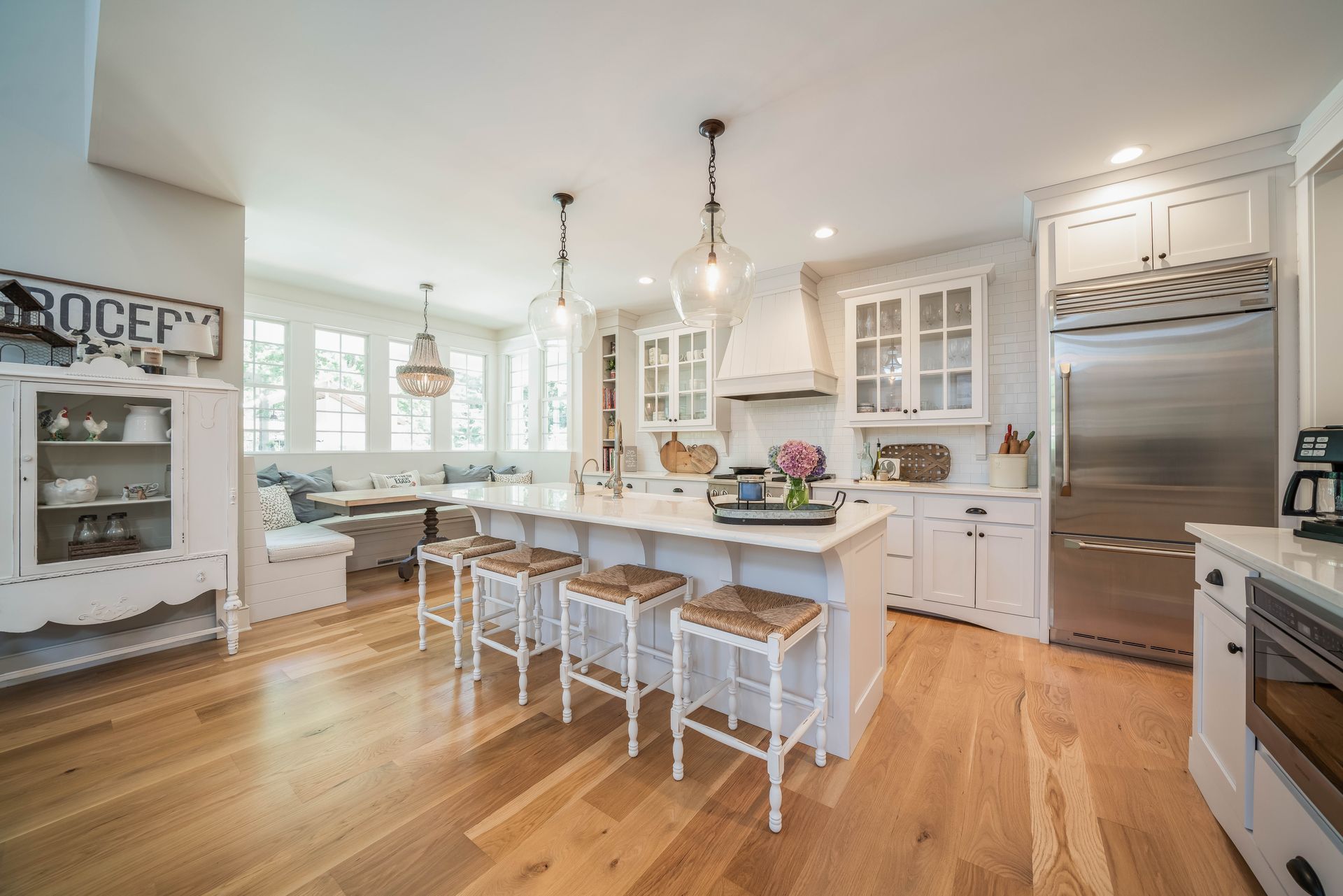 A kitchen with white cabinets , stainless steel appliances , hardwood floors and a large island.