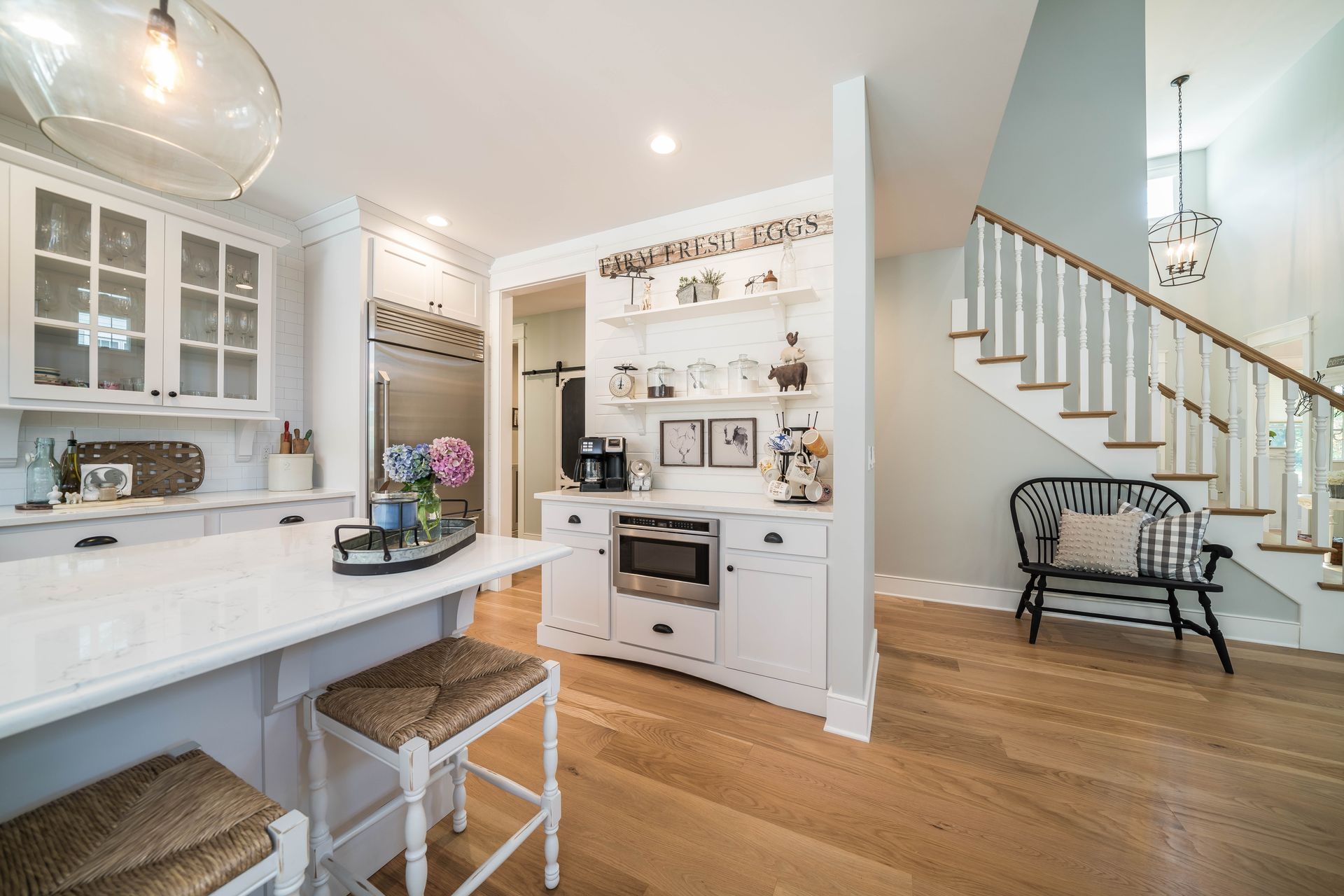 A kitchen with white cabinets and hardwood floors and a staircase in the background.