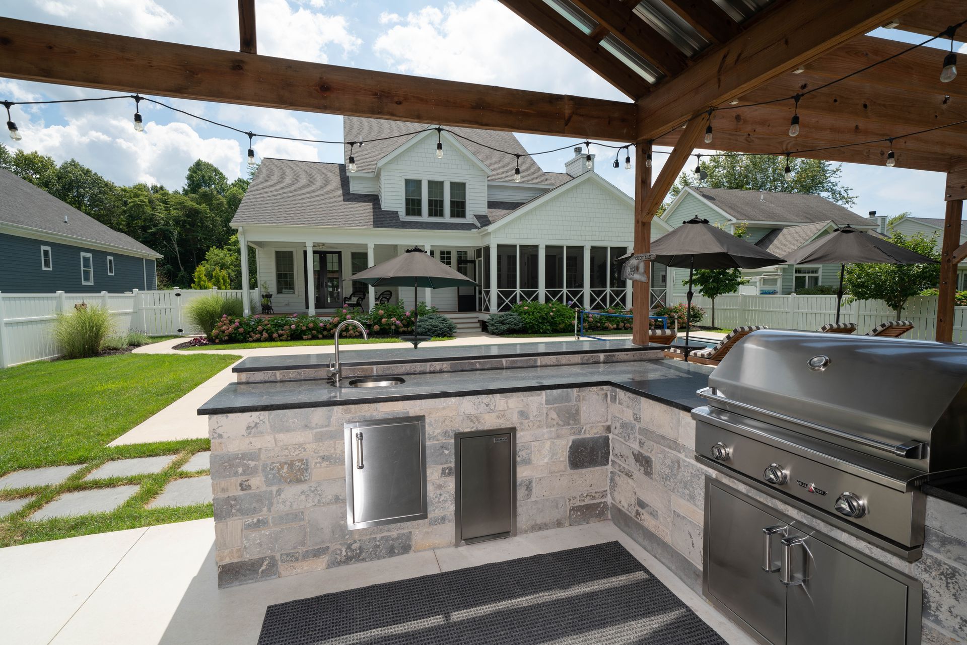 A large outdoor kitchen with a grill and umbrellas in front of a house.