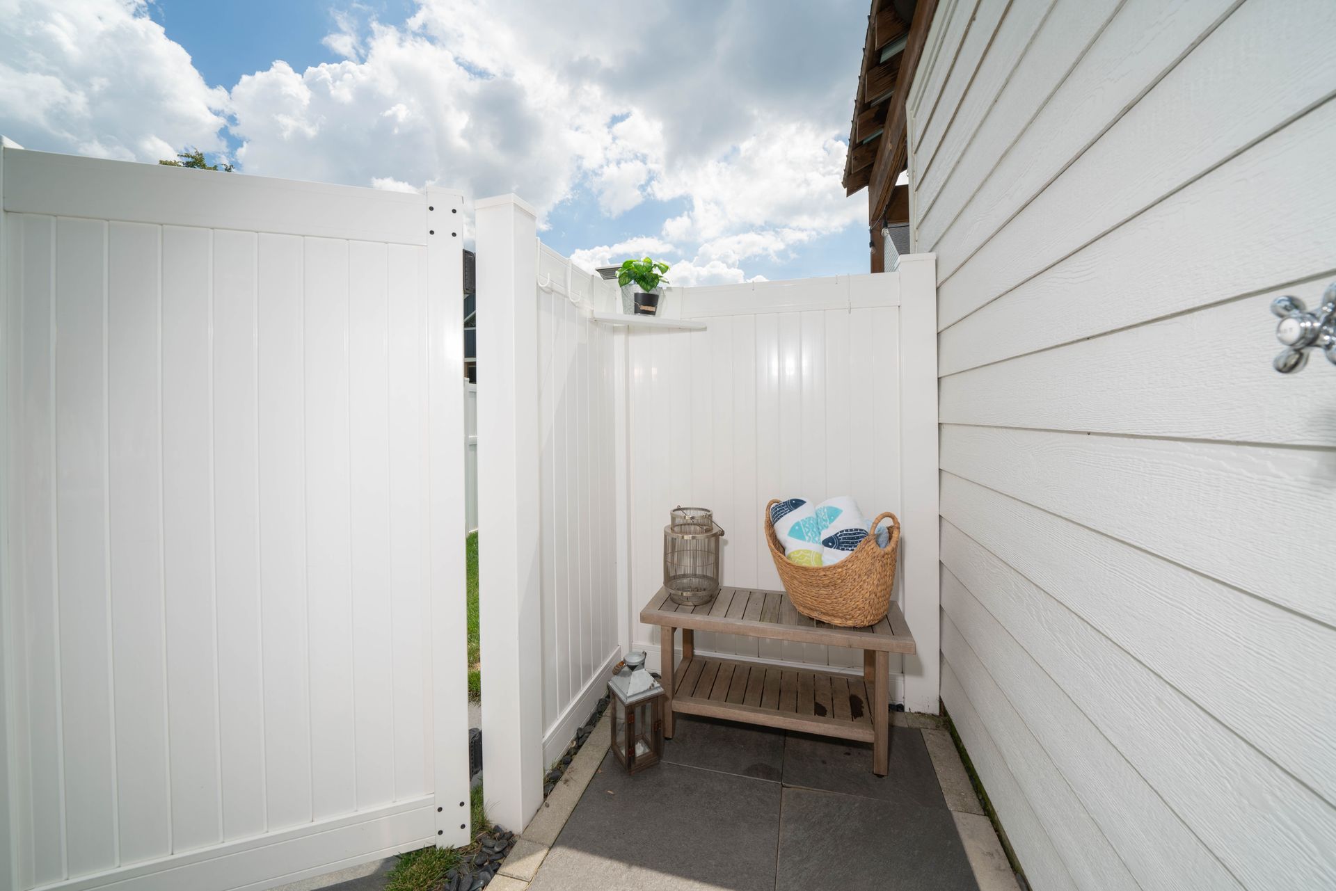 A white fence surrounds a patio area with a bench and a basket.