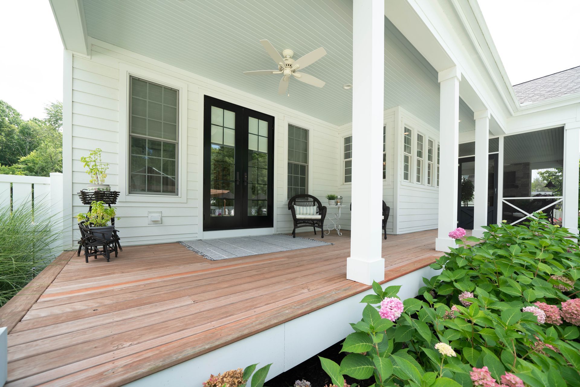 There is a porch with a ceiling fan and a chair on it.