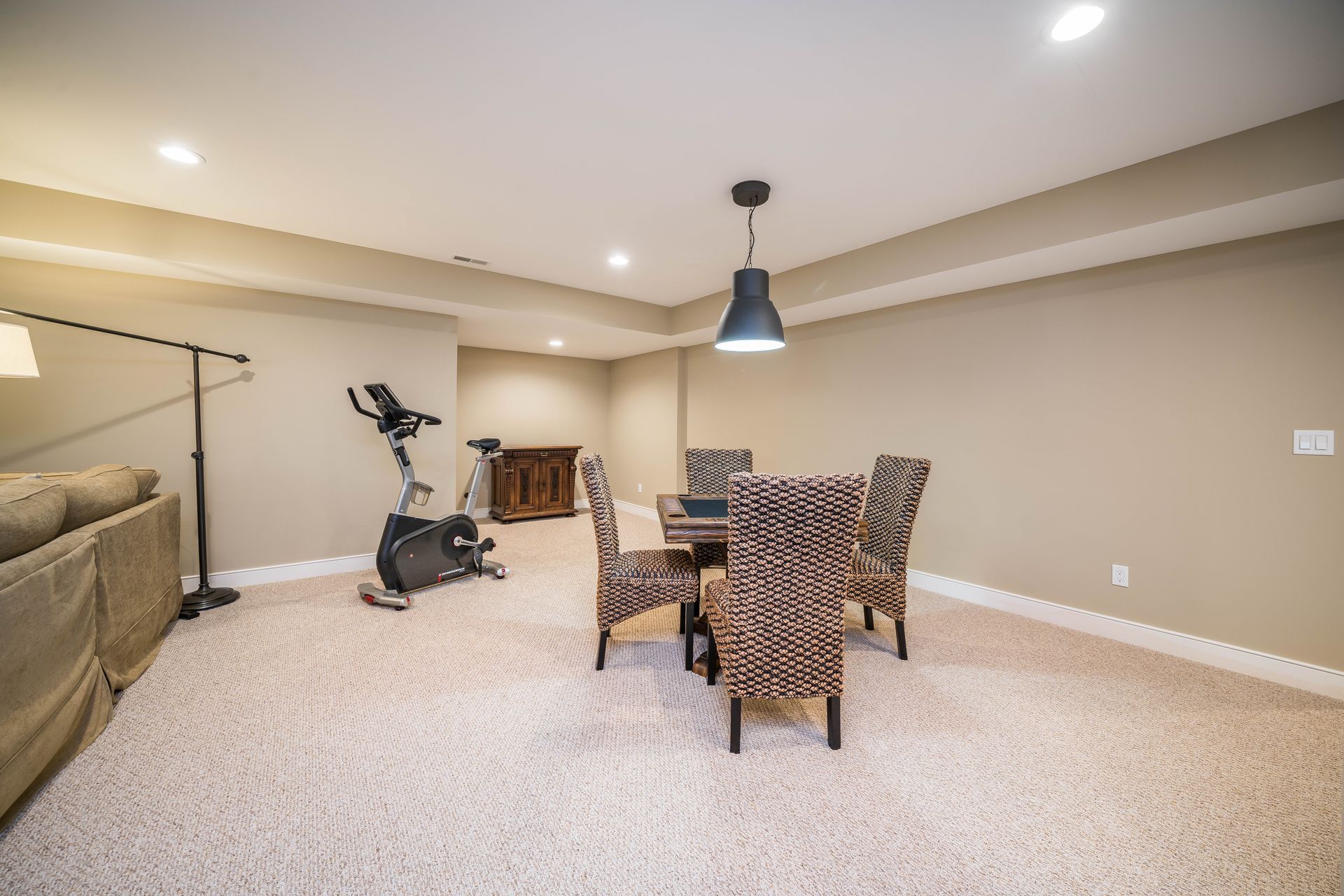 A basement with a table and chairs , a couch , and a bicycle.