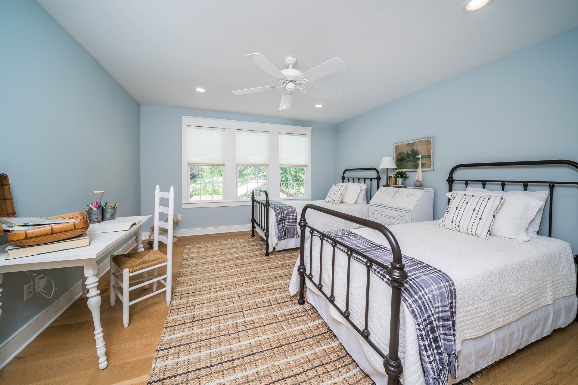 A bedroom with two beds , a desk , chairs and a ceiling fan.