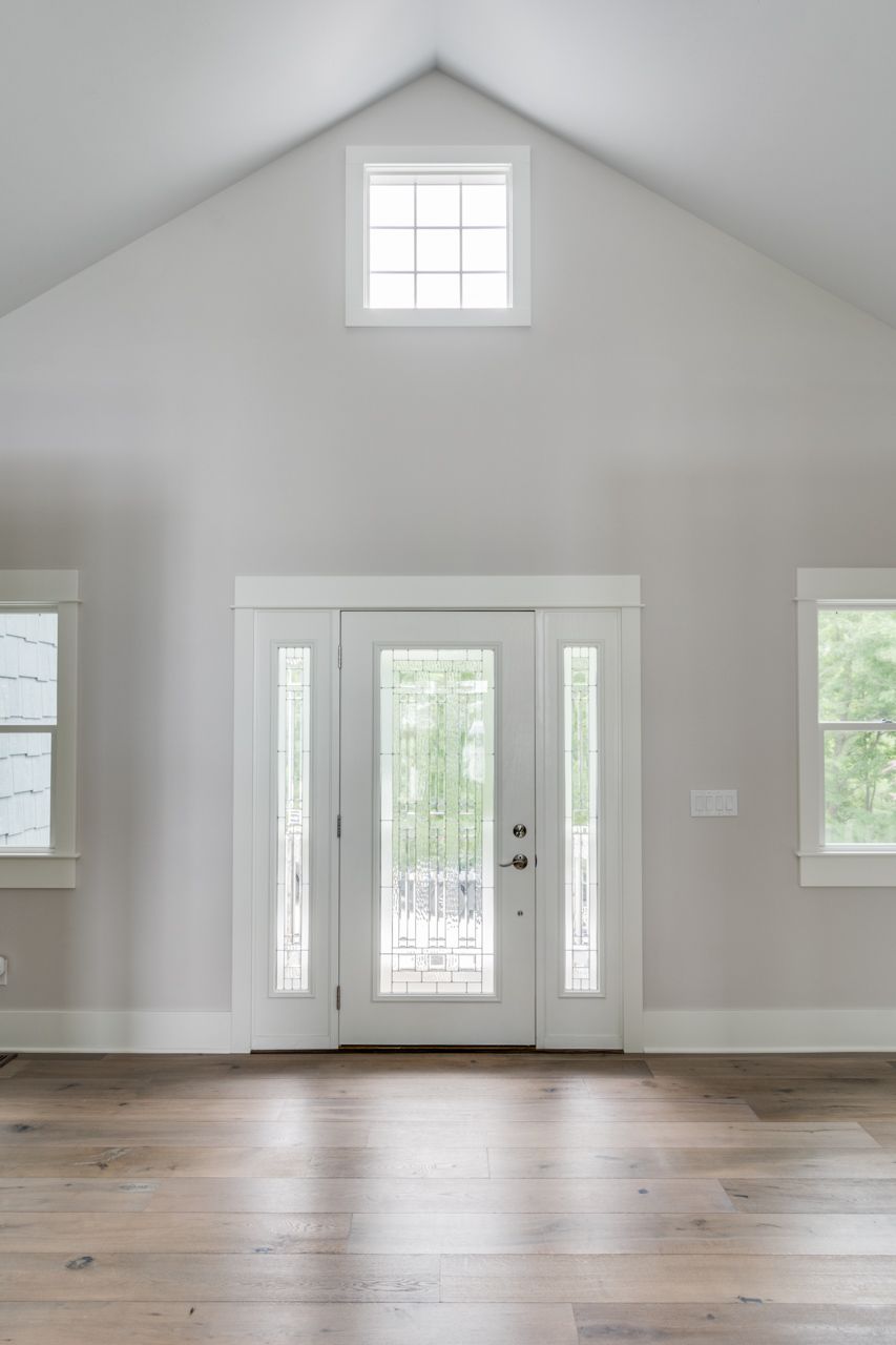 An empty living room with a vaulted ceiling , hardwood floors , and a door.
