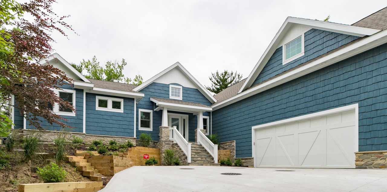 A large blue house with a white garage door is sitting on top of a hill.