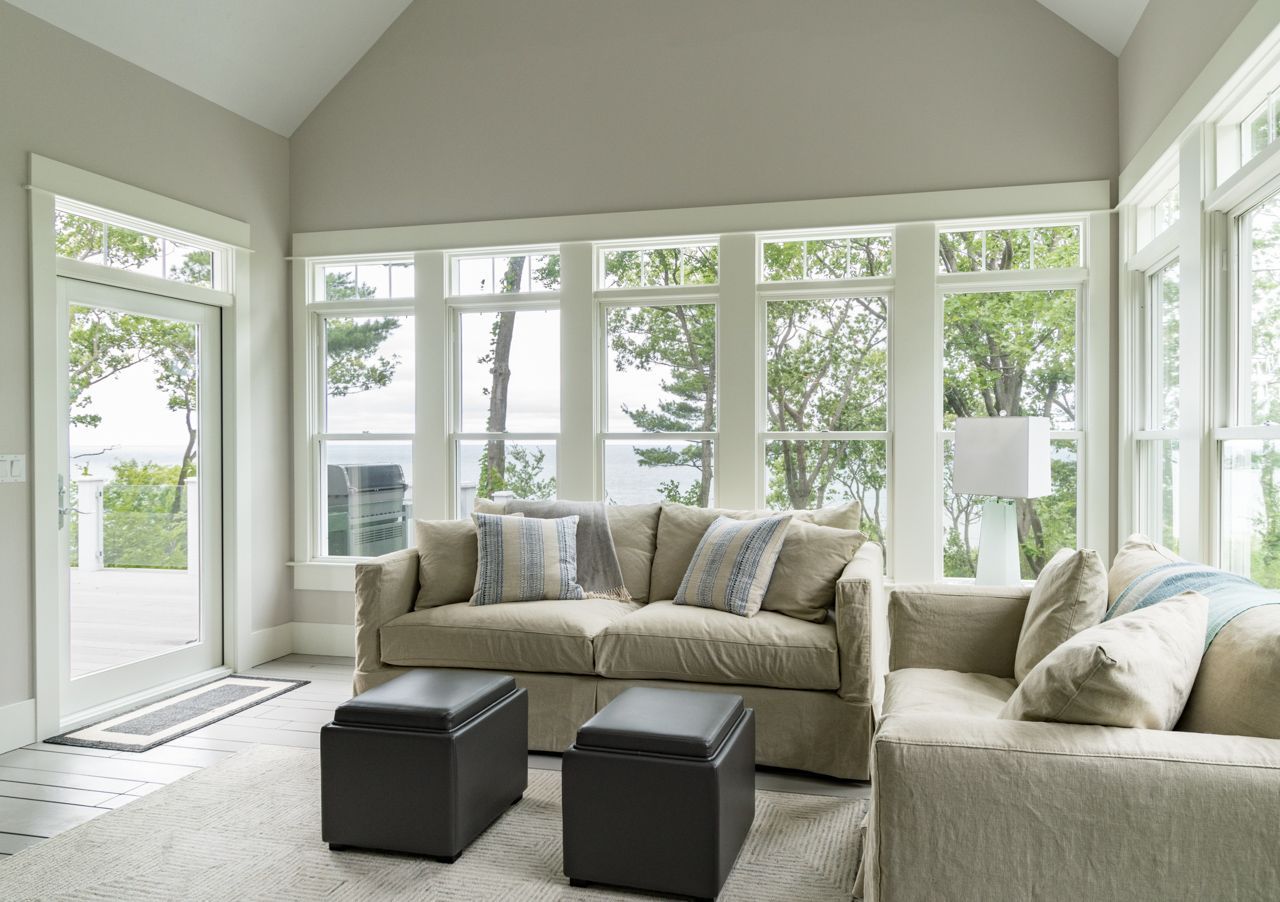 A living room with a couch , two ottomans , and lots of windows.