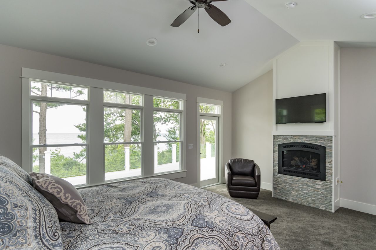 A bedroom with a bed , chair , fireplace and ceiling fan.