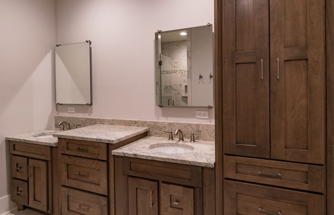 A bathroom with two sinks , two mirrors , and wooden cabinets.