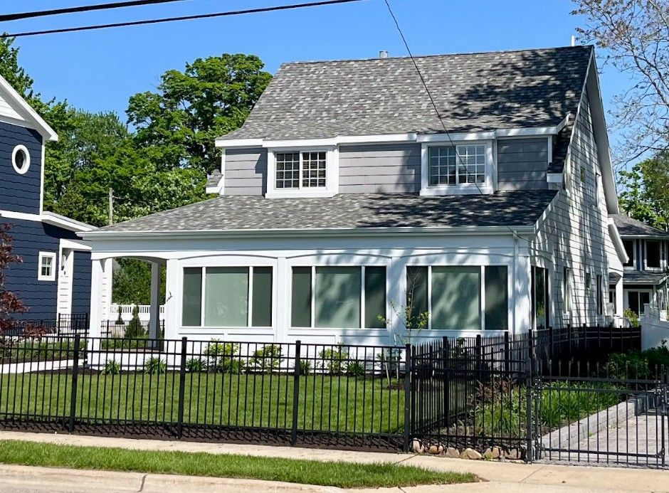 Gray and white house with black fence, trees, and blue sky.