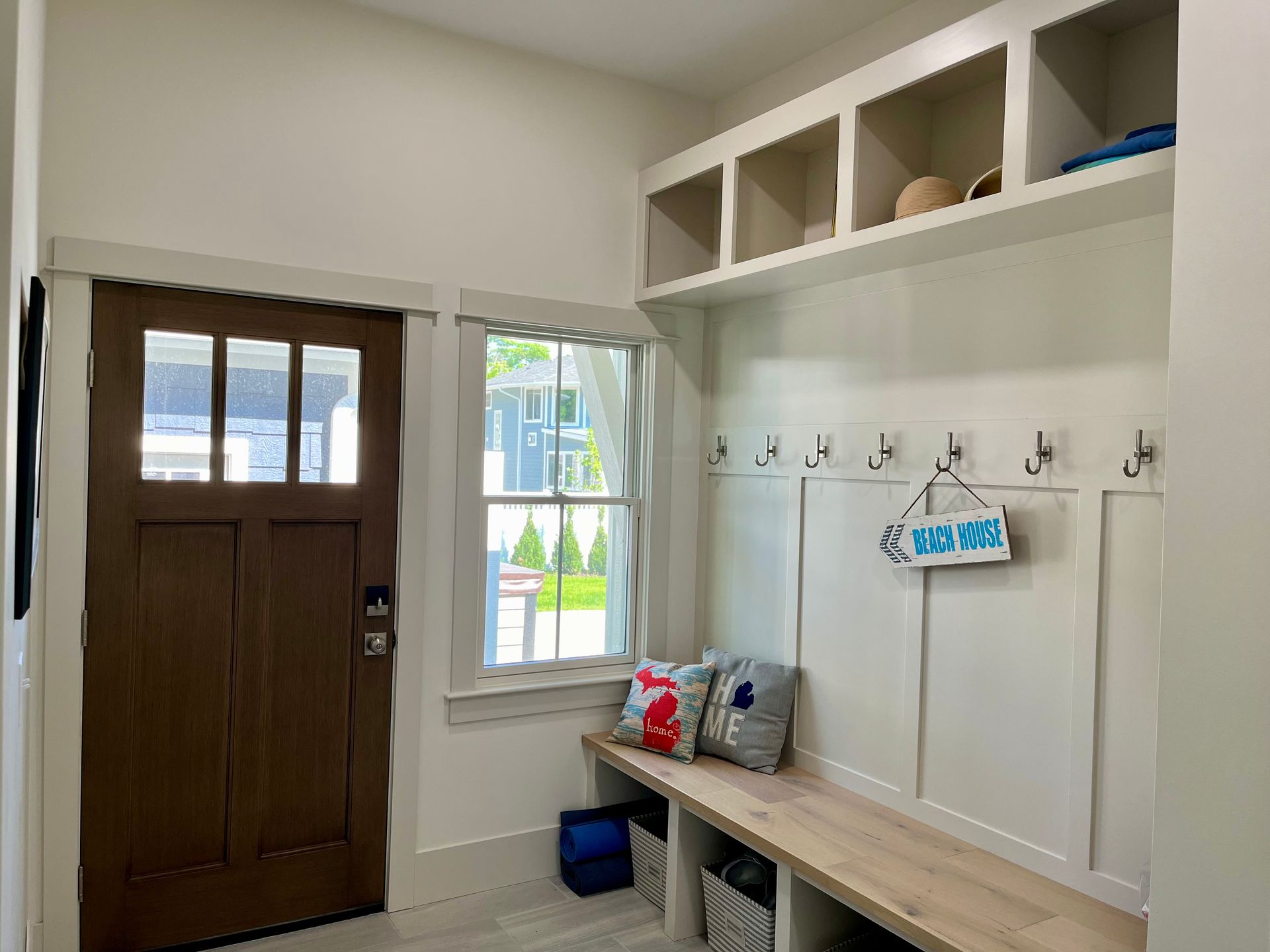 A mud room with a bench , hooks , shelves and a window.