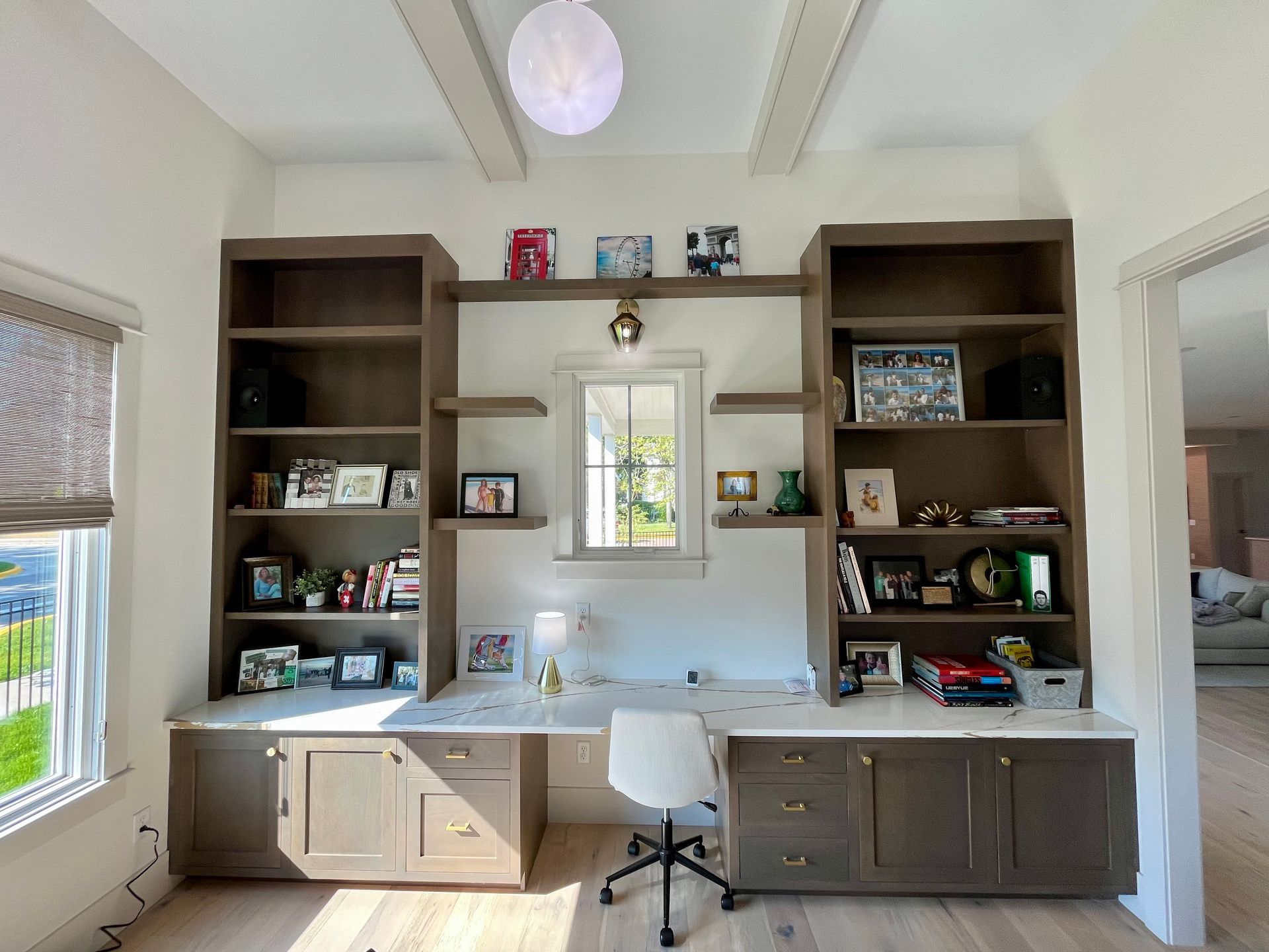 A home office with a desk , shelves , and a window.