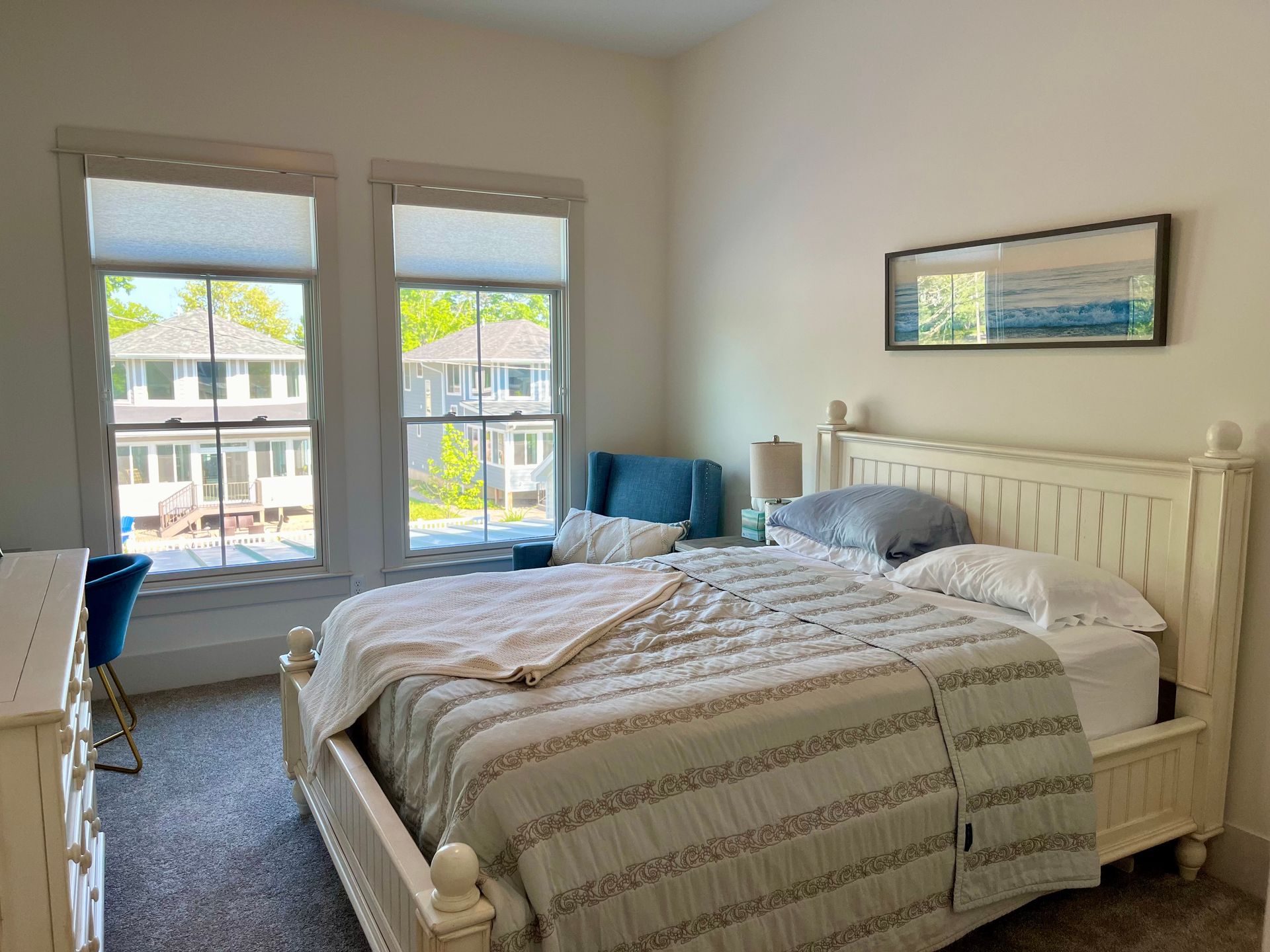 A bedroom with a bed , dresser , chair and two windows.