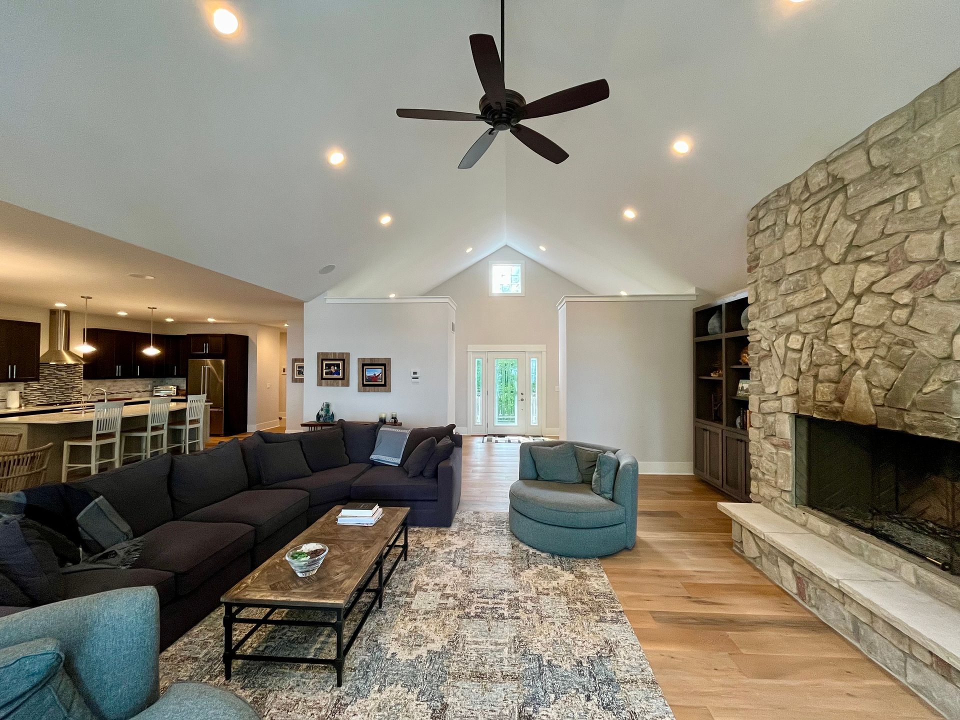 A living room with a couch , chair , coffee table , fireplace and ceiling fan.
