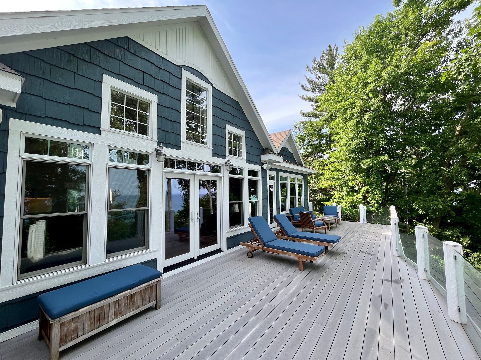 A large house with a large deck with chairs and a bench.